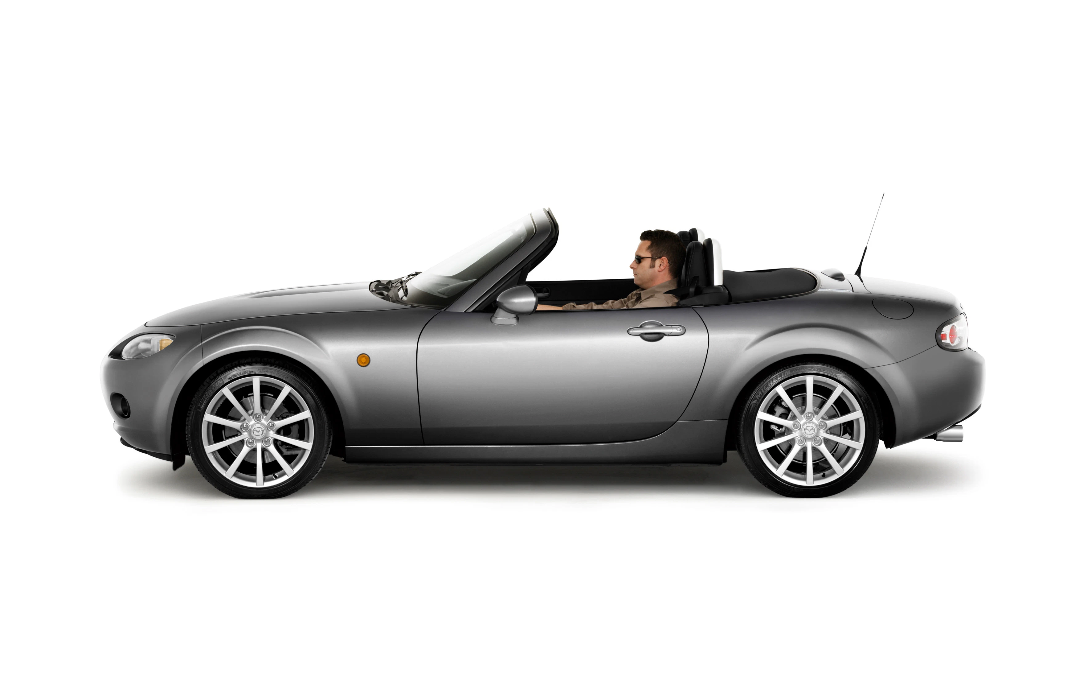 Silberner Cabrio-Sportwagen mit offenem Verdeck, Seitenansicht. Fahrer sitzt am Steuer. Weißer Hintergrund.