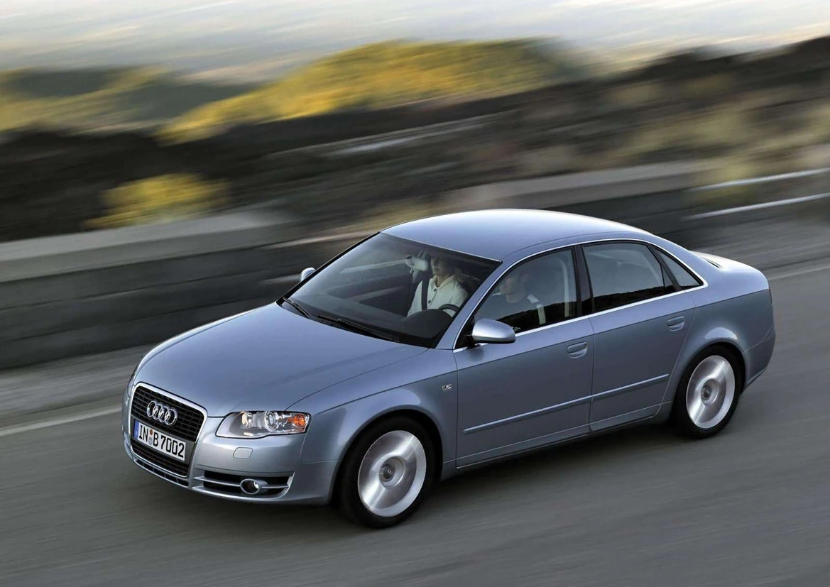 Silberner Audi A4 Limousine fährt auf einer kurvigen Straße in einer hügeligen Landschaft.