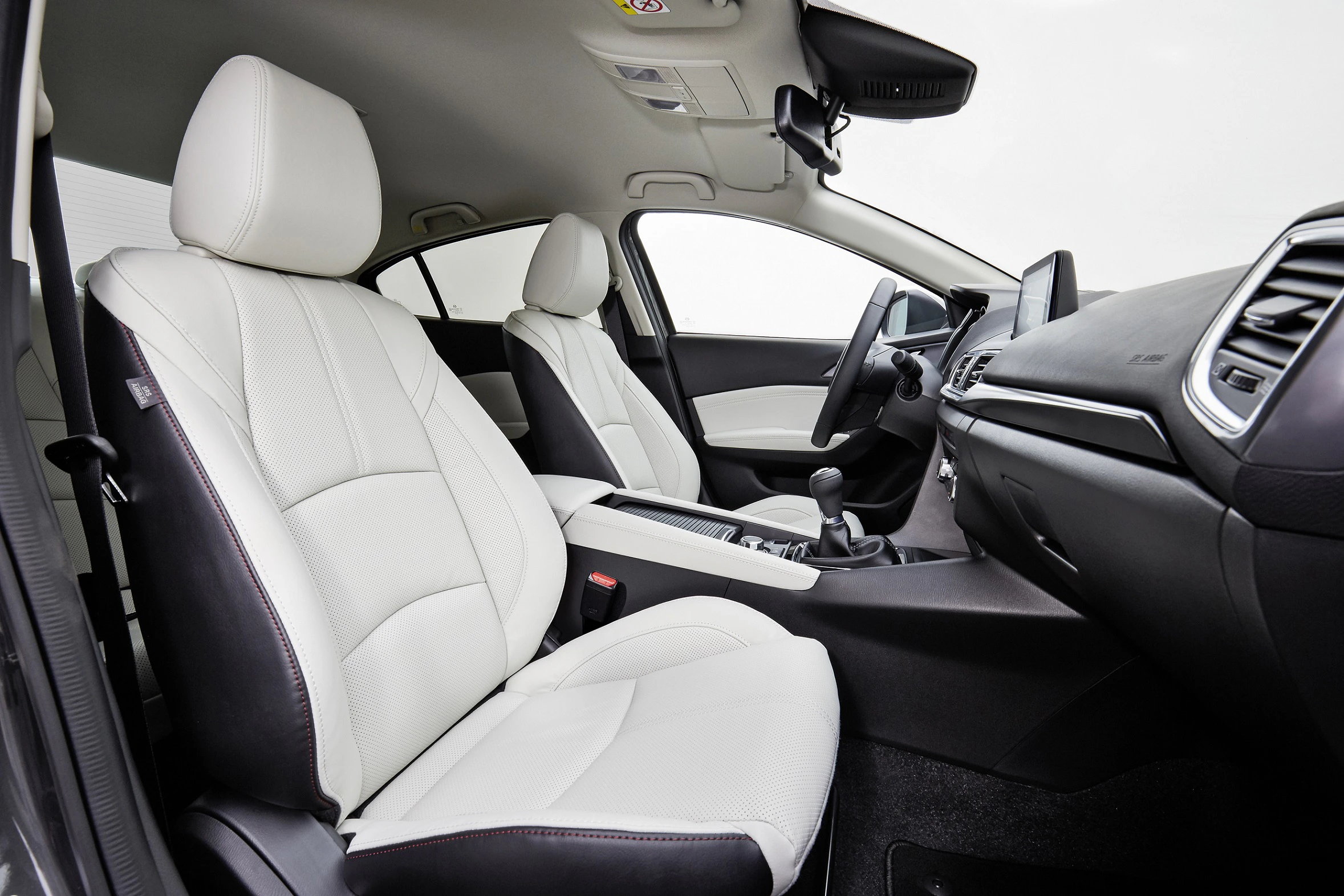 Innenraum eines modernen Autos mit weißen Ledersitzen, schwarzem Armaturenbrett und manuellem Getriebe, von der Seite fotografiert.