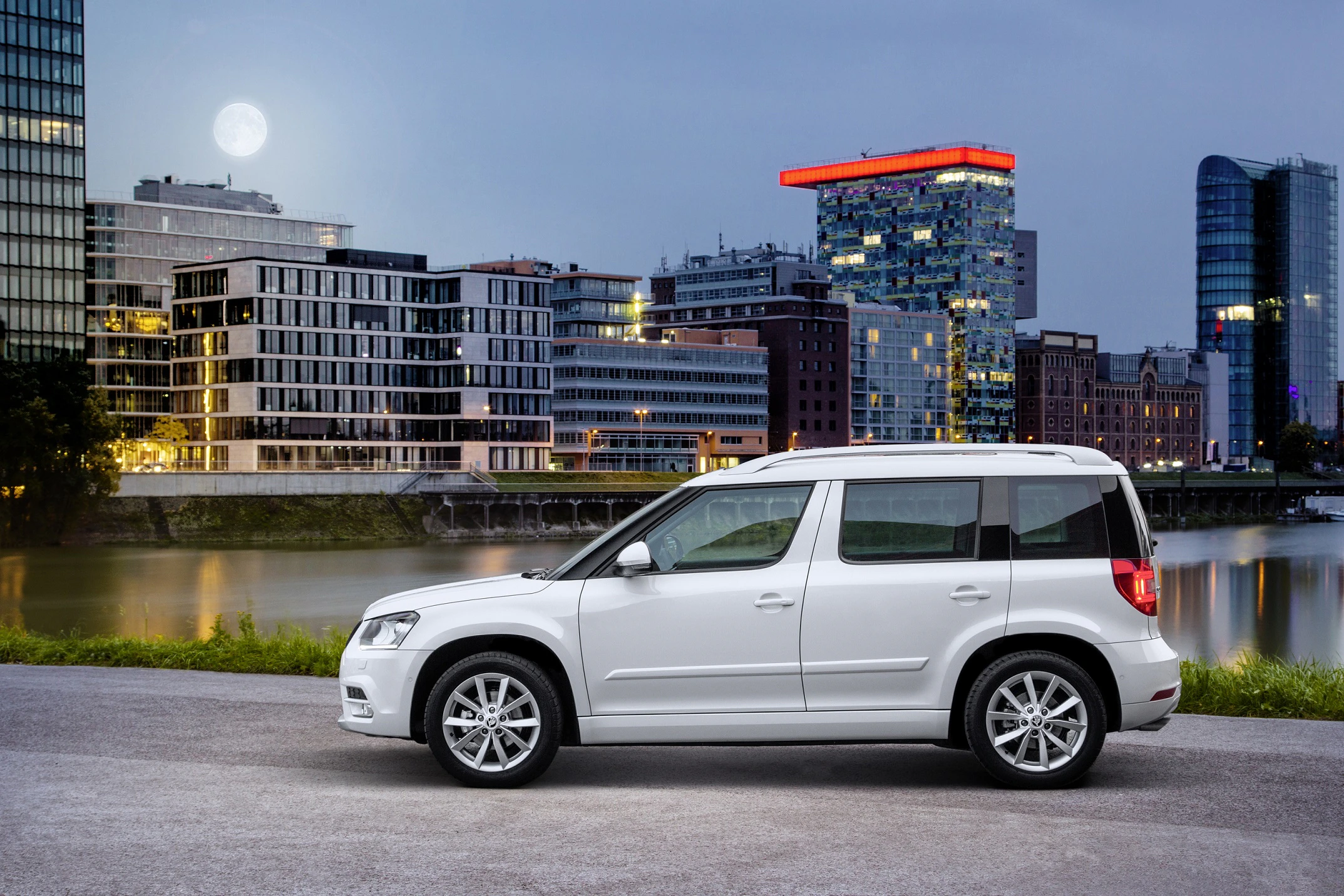 Weißer SUV vor einer städtischen Kulisse mit modernen Gebäuden und beleuchtetem Vollmond.