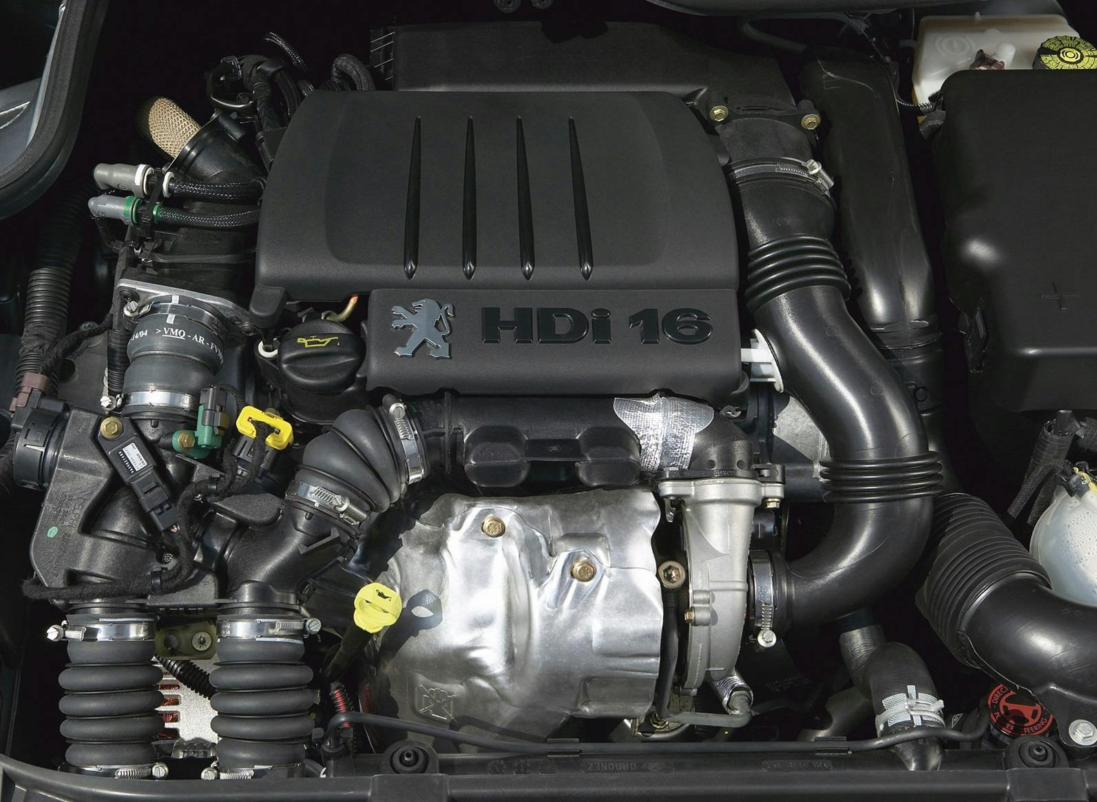 Nahaufnahme eines HDi 16 Dieselmotors in einem Auto mit verschiedenen sichtbaren Komponenten und dem Peugeot-Logo auf der Abdeckung.