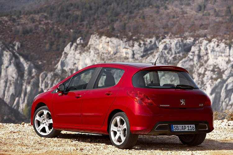 Roter Peugeot 308 parkt vor einer felsigen Berglandschaft unter klarem Himmel.