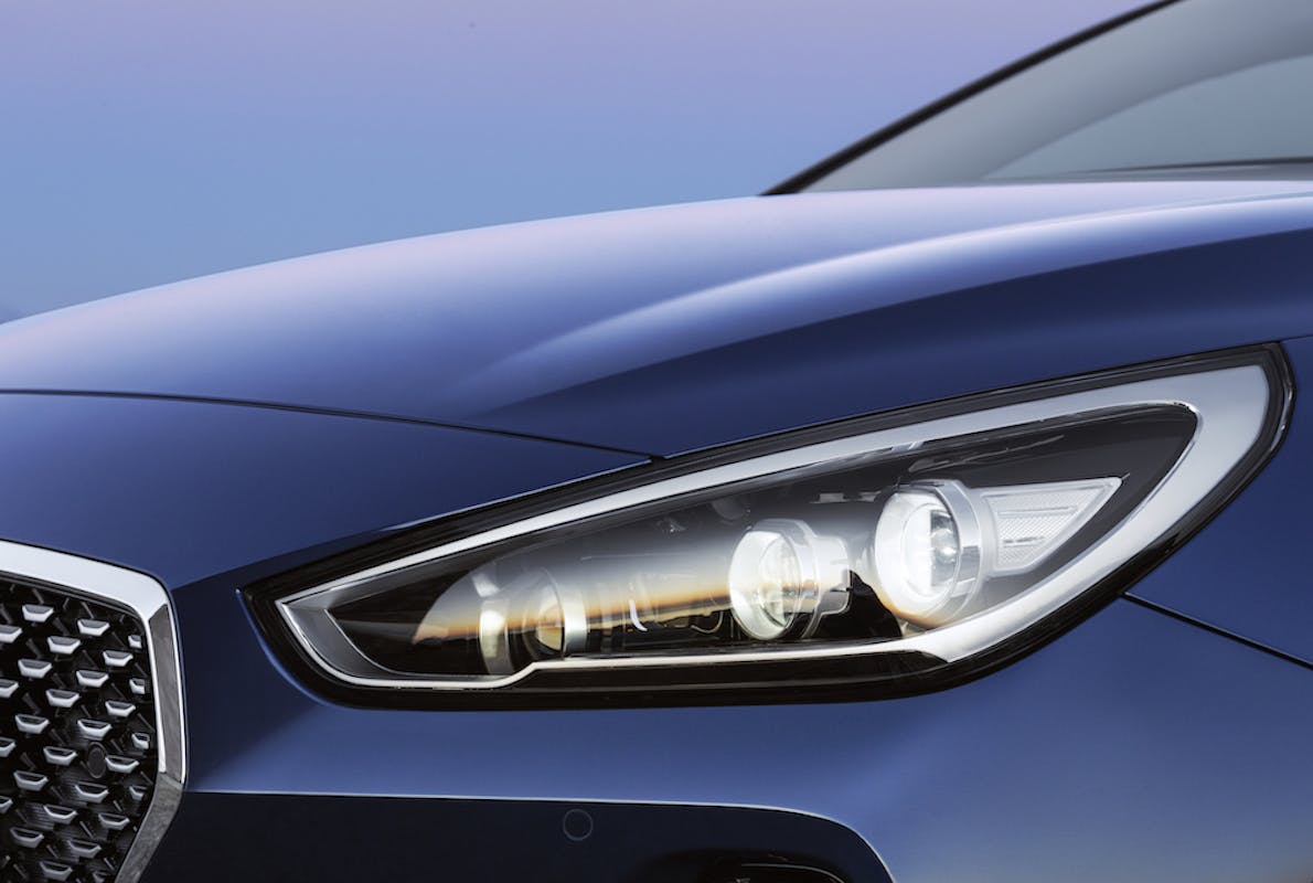 Nahaufnahme eines blauen Autos mit modernem Scheinwerferdesign und elegantem Kühlergrill vor einem blauen Himmel.