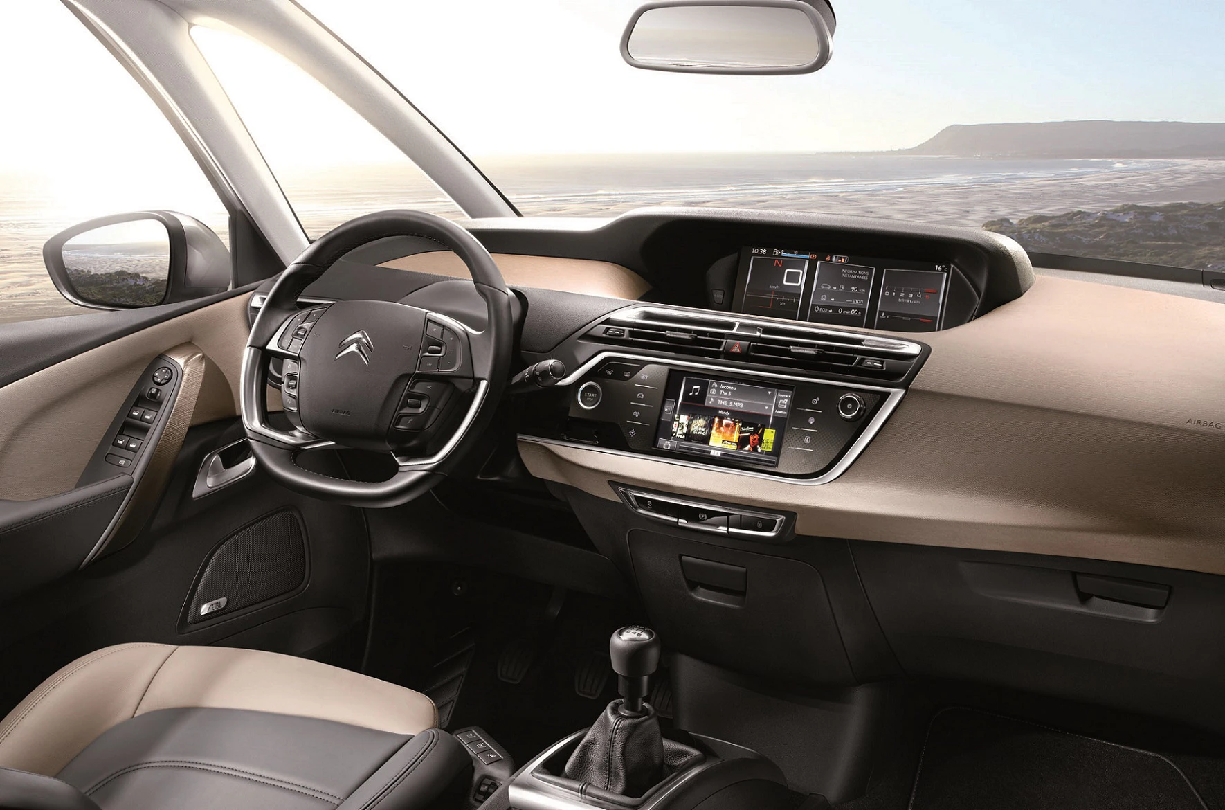Innenraum eines Autos mit modernem Armaturenbrett, Lenkrad und Touchscreen-Display. Im Hintergrund ist die Küste sichtbar.