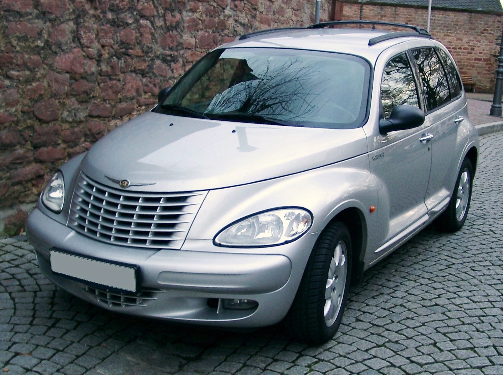 Silberner Chrysler PT Cruiser, geparkt auf gepflasterter Straße vor einer Steinmauer. Fahrzeug von schräg vorne abgebildet.