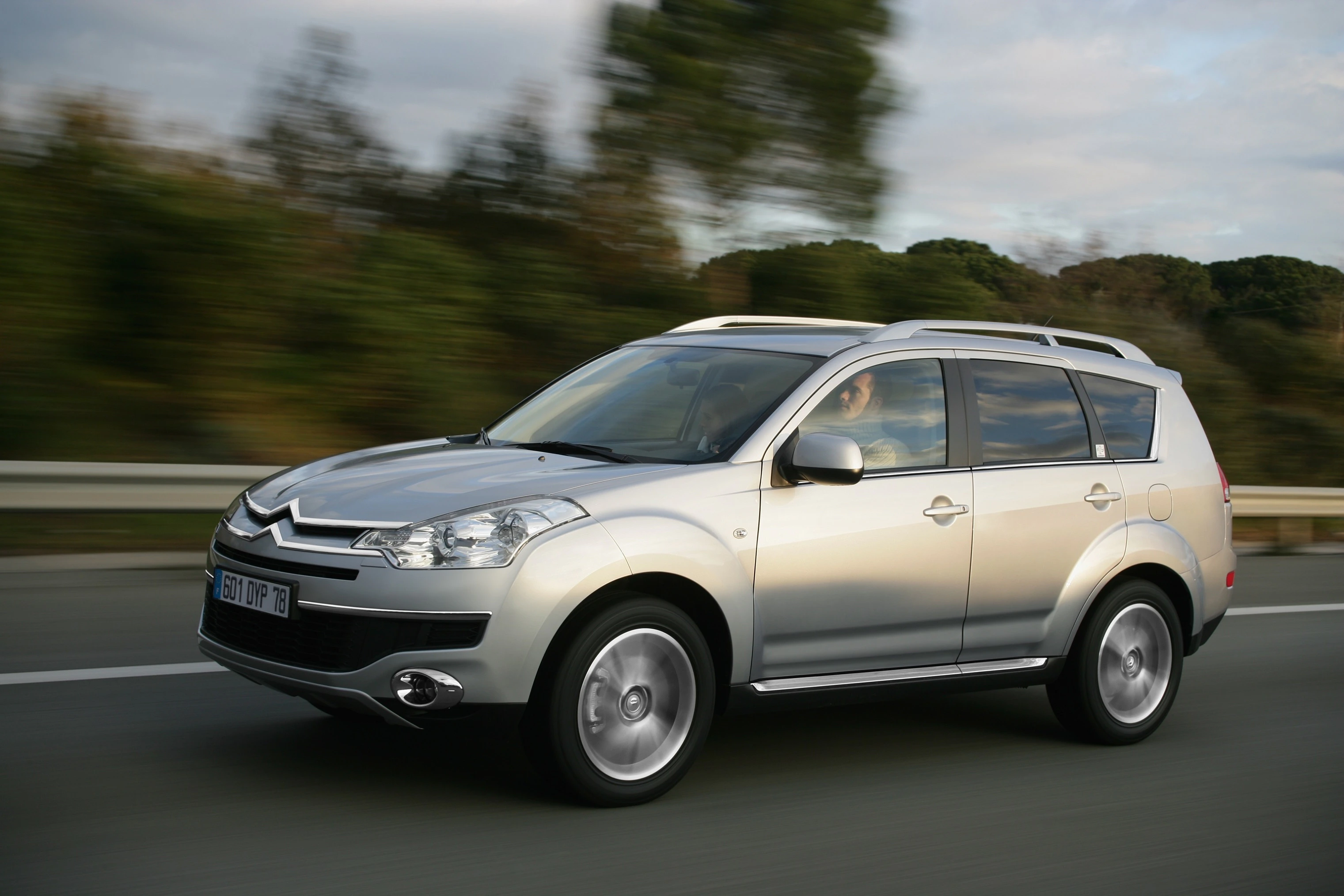 Silberner Citroën SUV fährt auf einer Autobahn, unscharfer Hintergrund mit Bäumen und Himmel, Auto von der Seite gesehen.