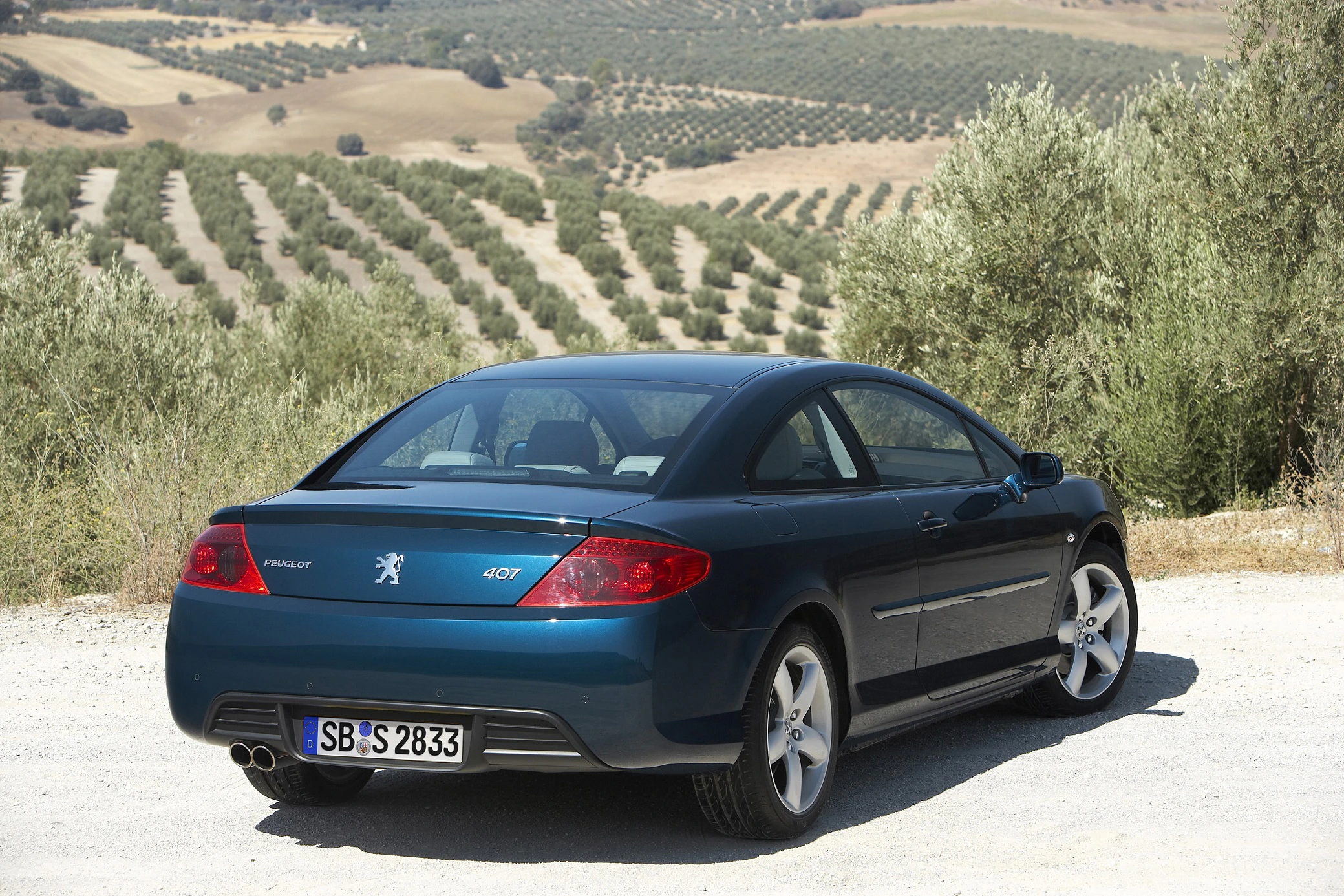 Peugeot 407 Coupé in einer ländlichen Landschaft mit Olivenbaumplantagen im Hintergrund.