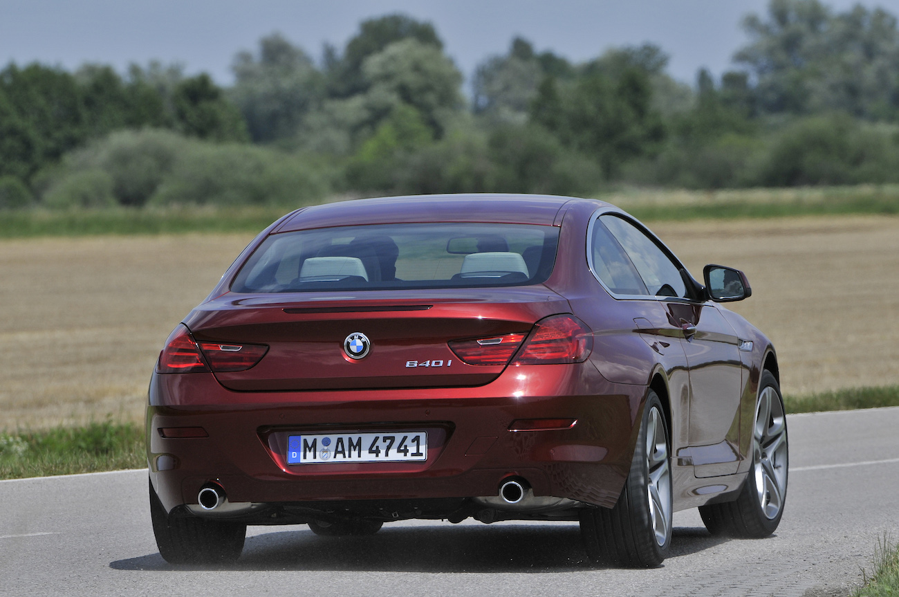 Rotes BMW-Coupé fährt auf einer Landstraße, umgeben von Feldern und Bäumen. Das Nummernschild zeigt "M AM 4741".