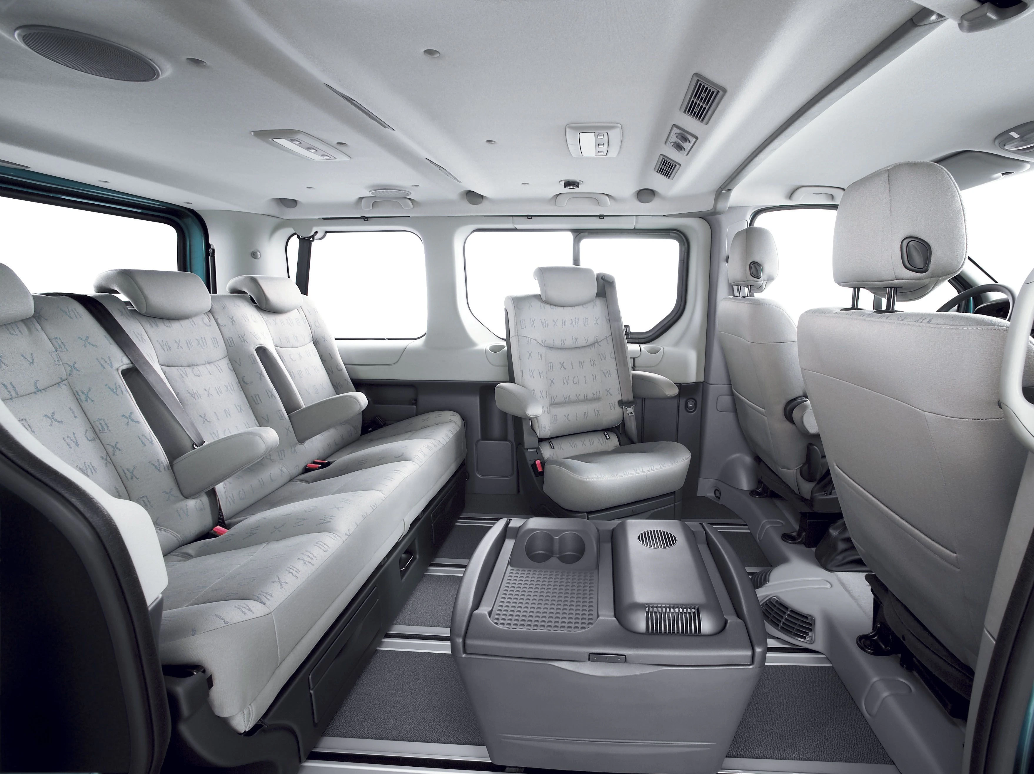 Innenraum eines geräumigen Vans mit grauen Sitzen und einem Tisch in der Mitte. Große Fenster bieten viel Licht.