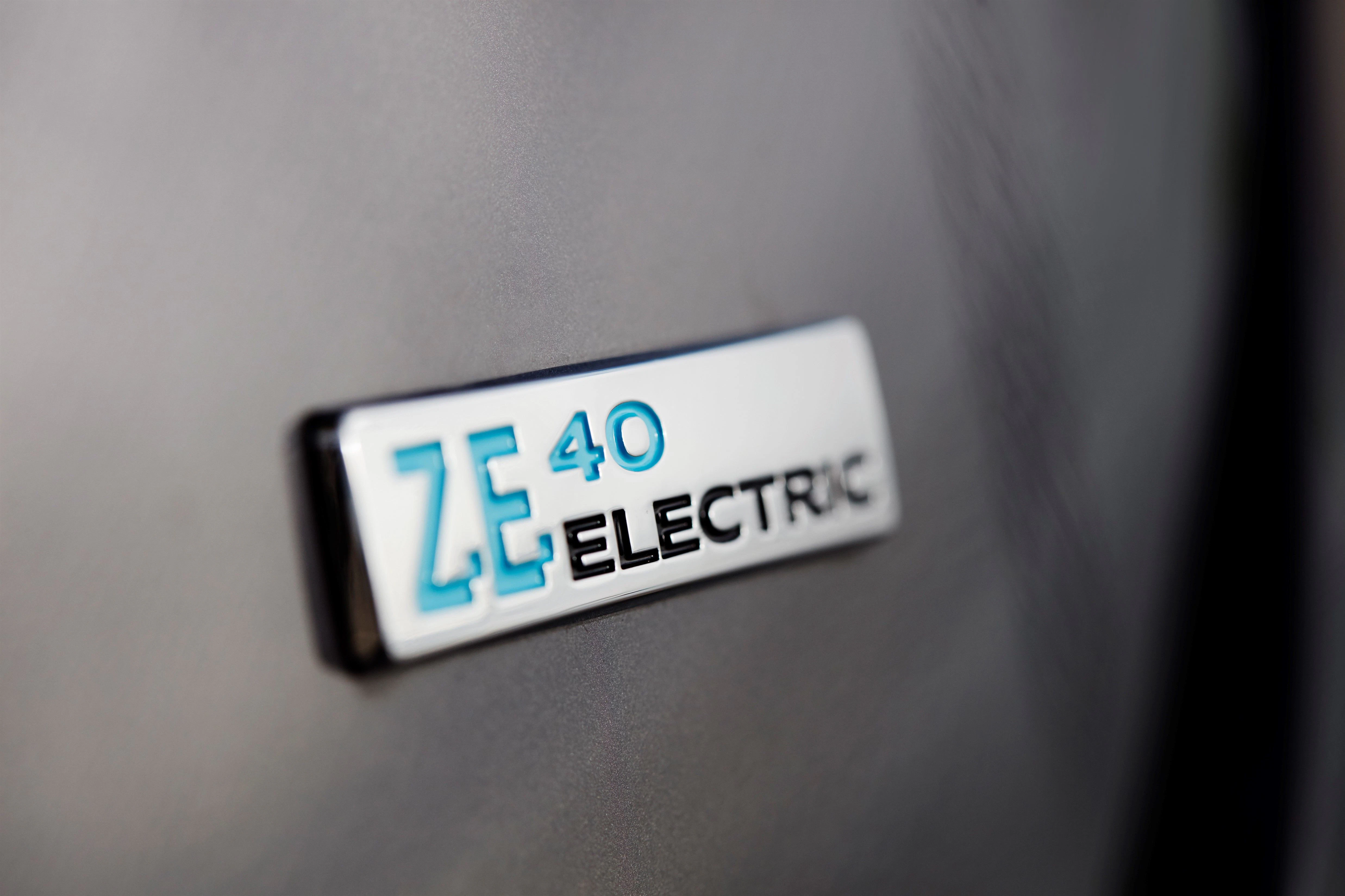 Nahaufnahme eines metallenen Emblems mit der Aufschrift "ZE 40 ELECTRIC" auf einer glatten, grauen Fahrzeugoberfläche.