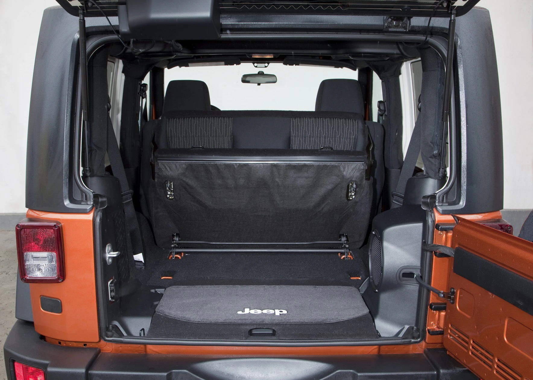 Geöffneter Kofferraum eines oranges Jeeps, Blick von hinten. Rücksitze hochgeklappt, Laderaum leer. Innenraum in Schwarz und Grau.