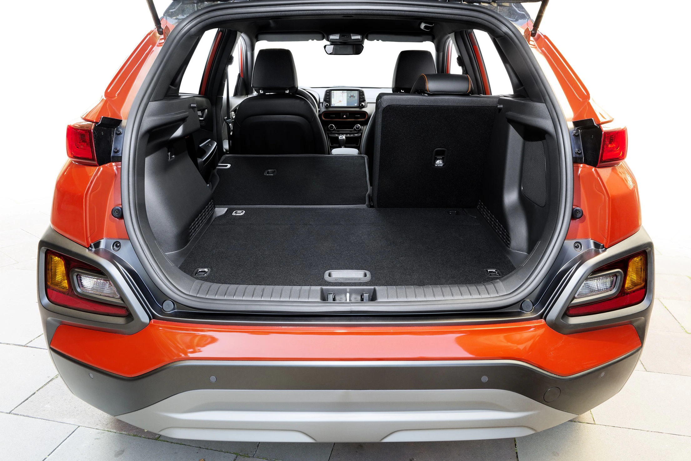 Offener Kofferraum eines orangefarbenen SUV, Rücksitze teils umgeklappt, geräumiger Innenraum erkennbar.