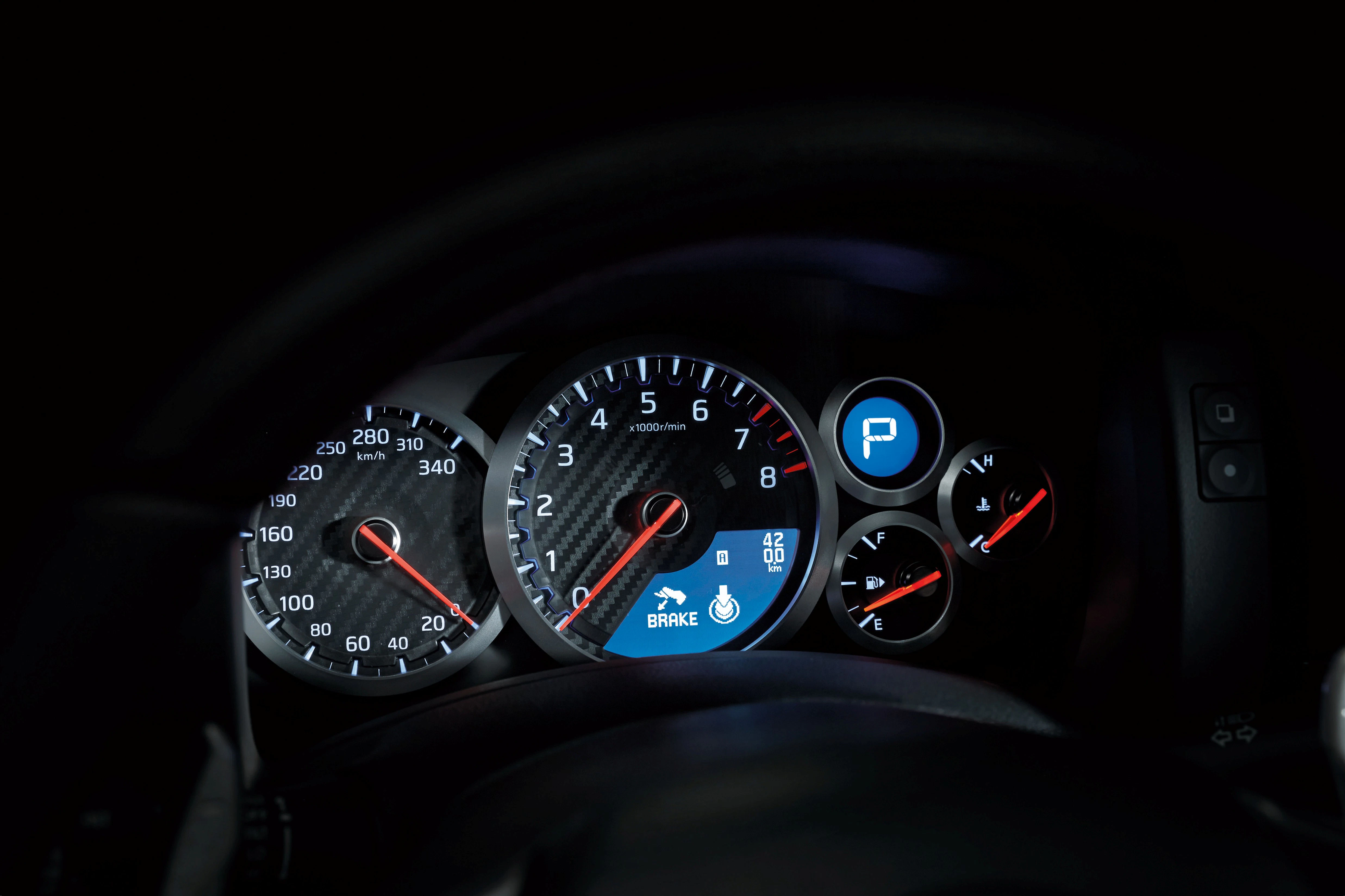 Nahaufnahme eines beleuchteten Tachometers mit Geschwindigkeitsanzeige, Drehzahlmesser und Tankanzeige in einem Auto bei Nacht.