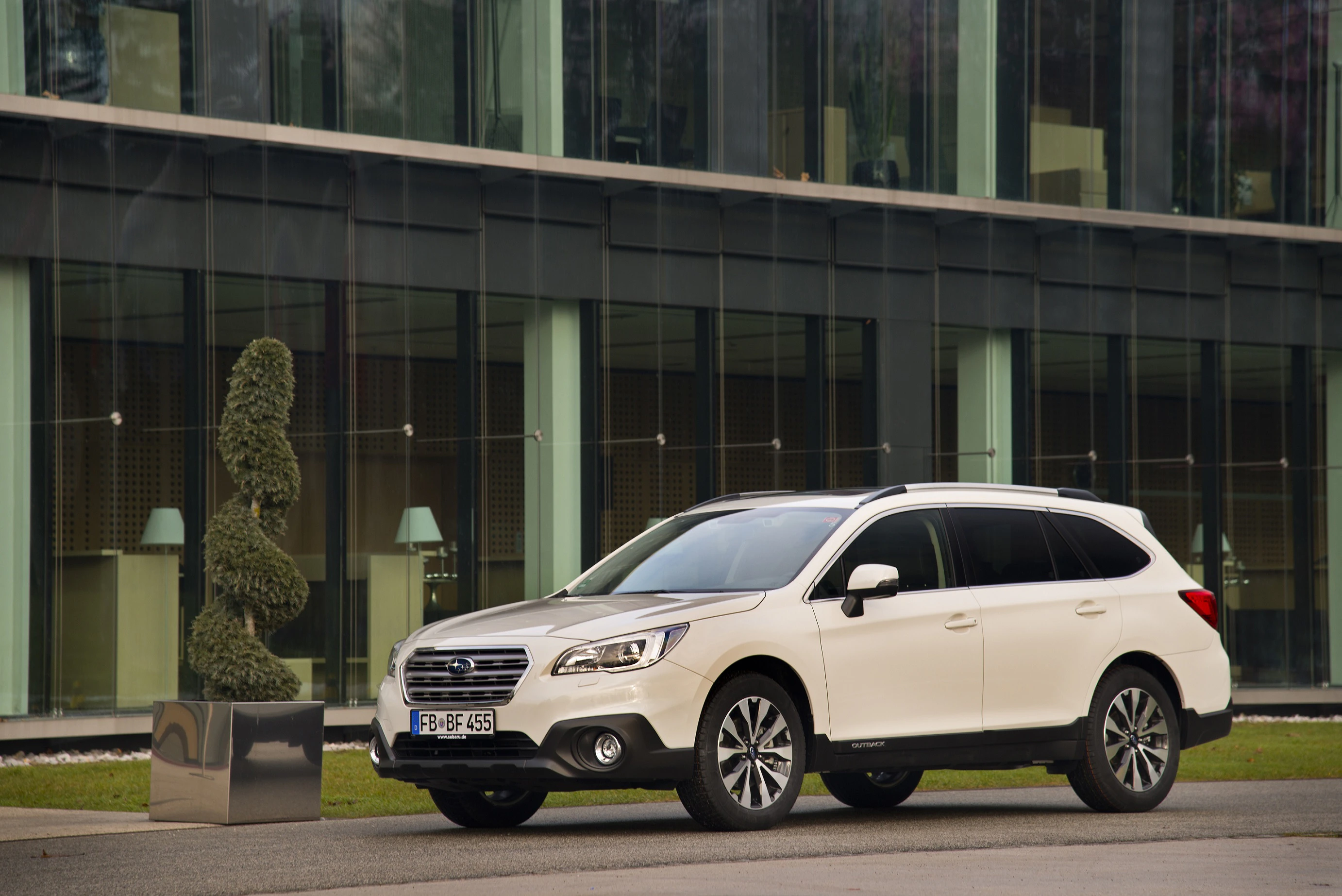 Weißer SUV parkt vor einem modernen Glasgebäude; klare Linien und stilvolle Architektur im Hintergrund.