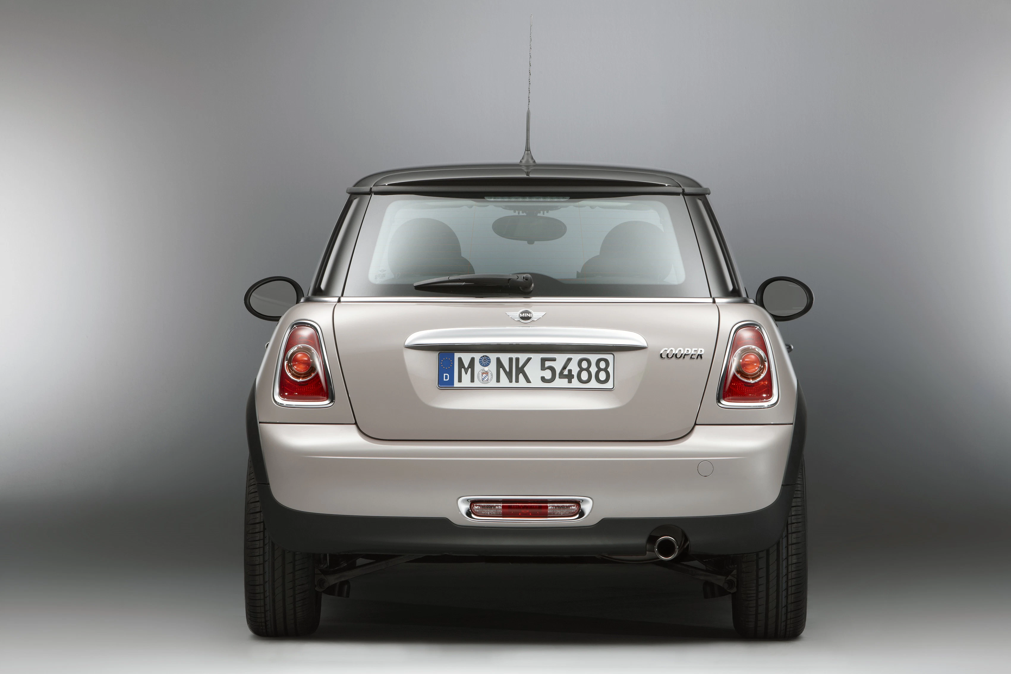 Ein silberner Mini Cooper von hinten, mit deutschem Kennzeichen "M NK 5488" vor einem grauen Hintergrund.