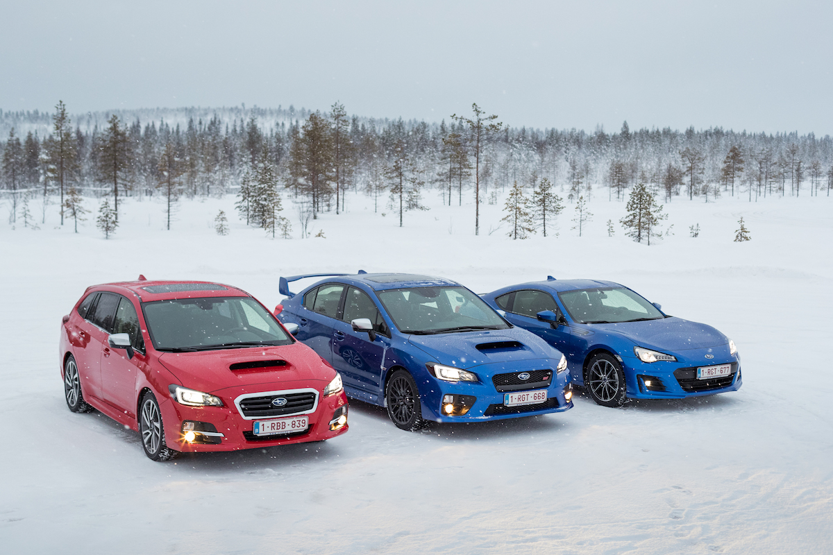 Drei bunte Subaru-Autos geparkt im Schnee, umgeben von einer verschneiten Landschaft mit schneebedeckten Bäumen im Hintergrund.