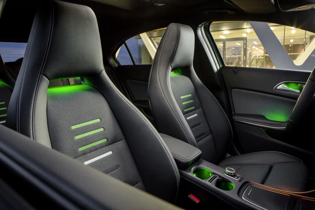 Innenansicht eines modernen Autos mit zwei Sportsitzen und grünem Ambiente-Licht, elegantes Design mit Mittelkonsole und Getränkehaltern.