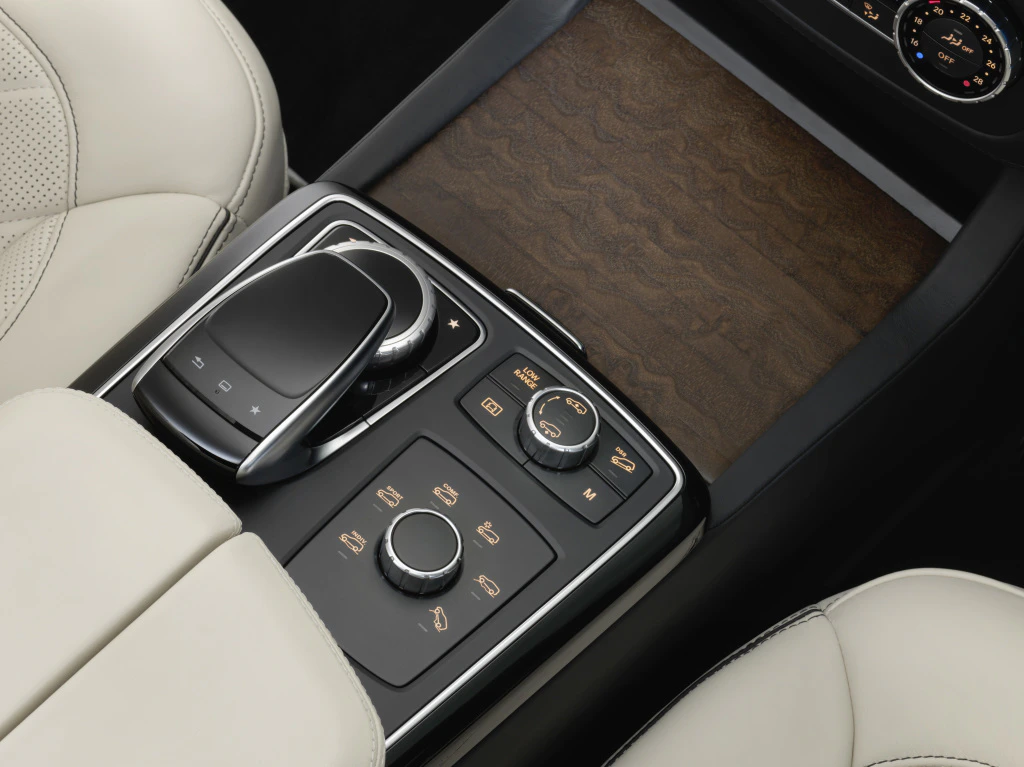 Nahaufnahme einer luxuriösen Auto-Mittelkonsole mit verschiedenen Bedienelementen und Holzverkleidung, umgeben von cremefarbenem Leder.