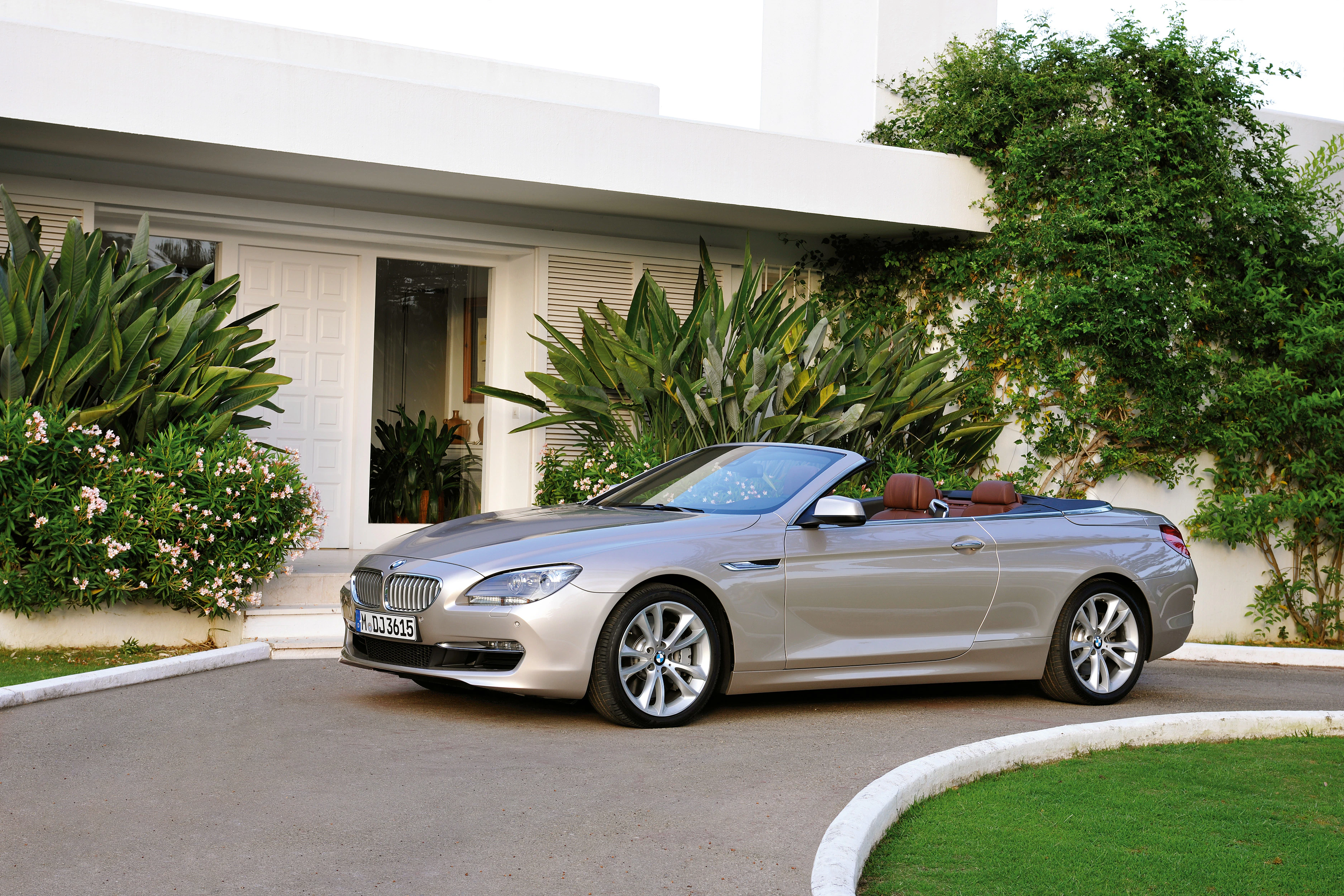 Silbernes Cabriolet parkt vor einem modernen Haus mit grünen Pflanzen. Elegantes Design, offenes Verdeck, luxuriöser Look.