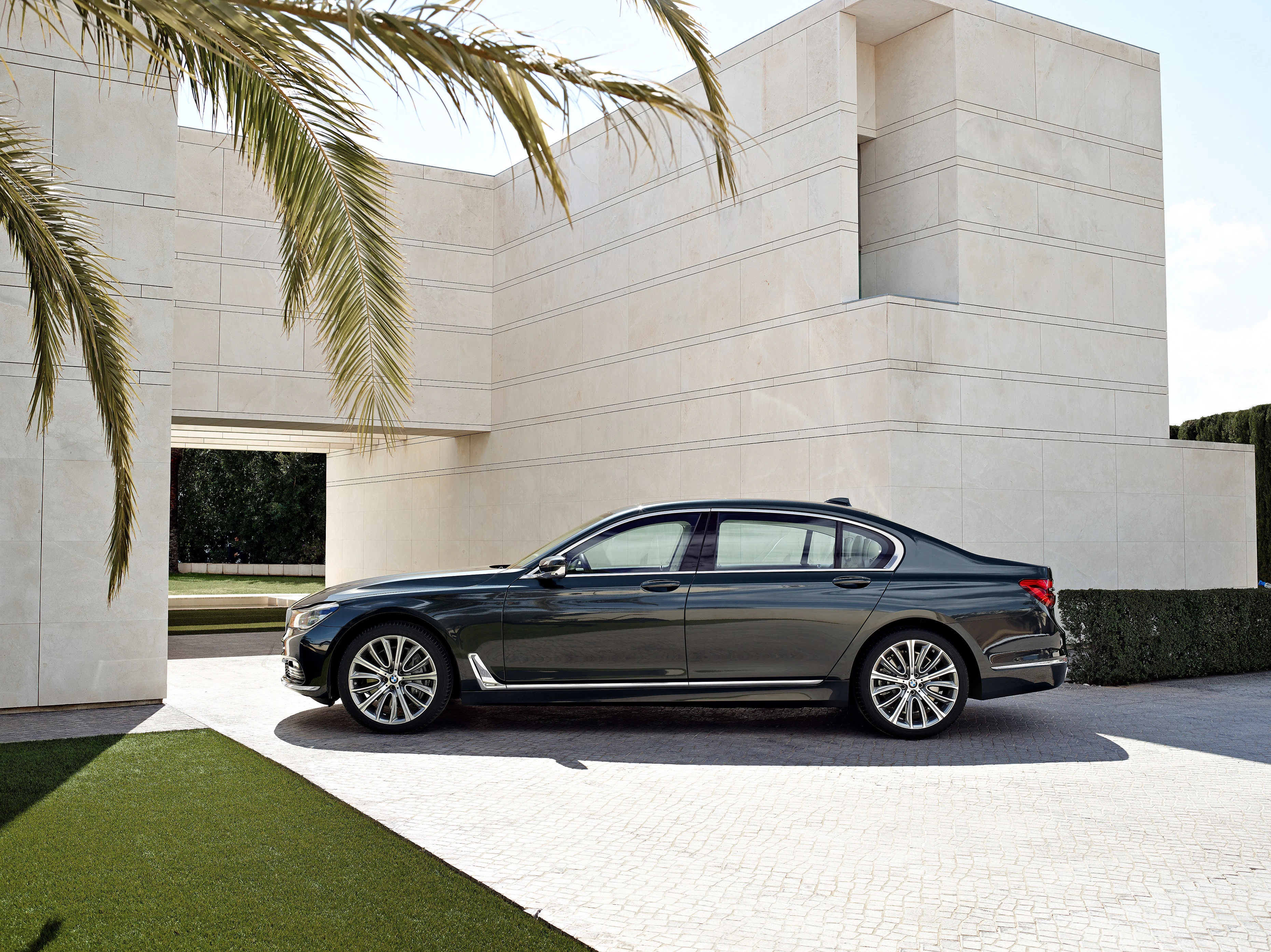 Luxuslimousine geparkt vor modernem, weißem Gebäude, umgeben von Palmen. Elegantes Design mit glänzender schwarzer Lackierung.