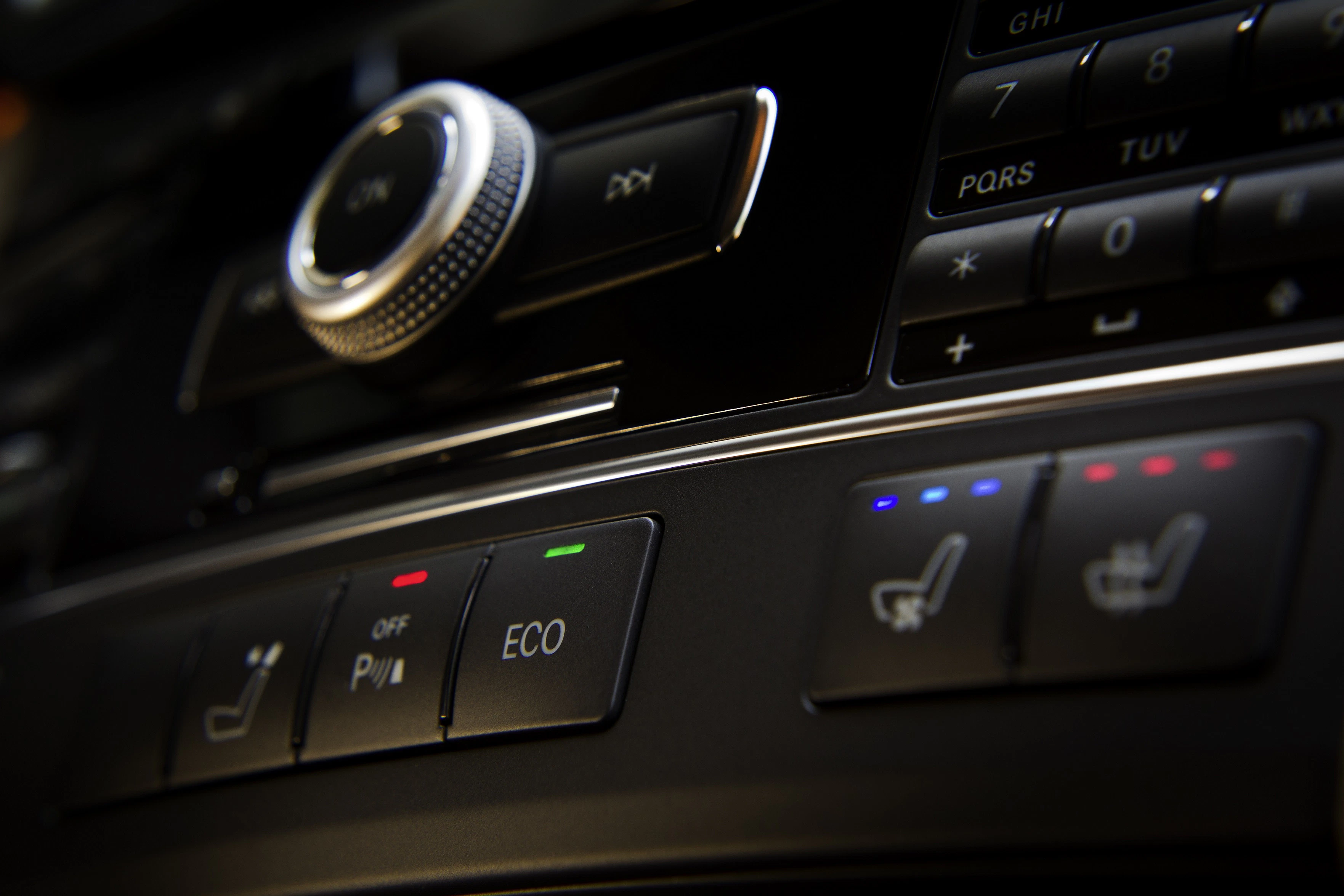 Nahaufnahme der Mittelkonsole eines Autos mit Tasten für Sitzheizung, ECO-Modus und einem Drehknopf.