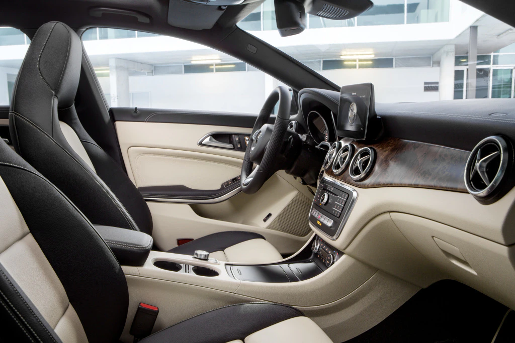 Innenraum eines modernen Autos mit hellem Lederinterieur, Holzverkleidung und digitalem Bildschirm auf der Mittelkonsole.