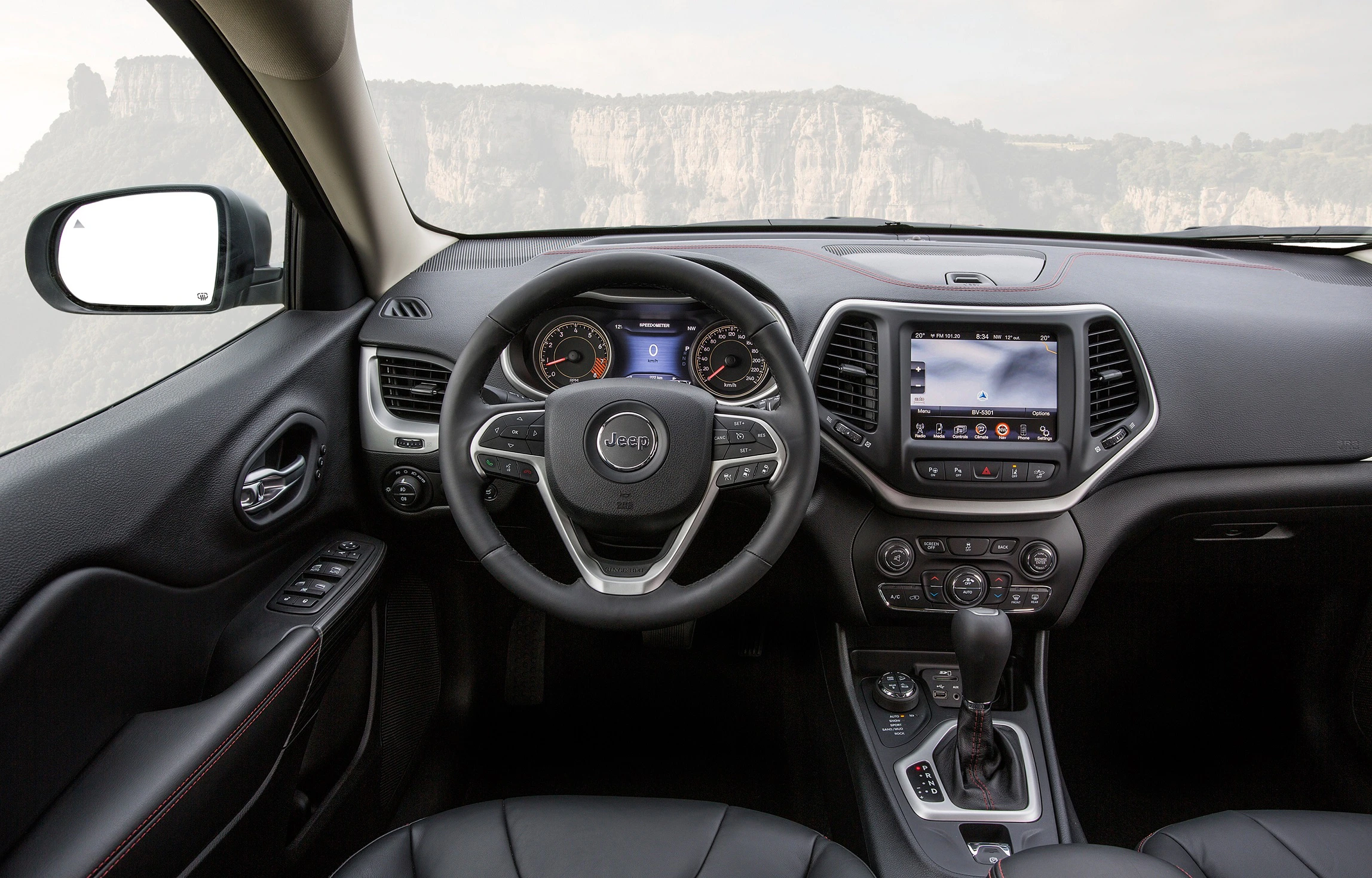Innenraum eines modernen Autos mit Lenkrad, Armaturenbrett und Infotainmentsystem. Durch die Windschutzscheibe sieht man eine Berglandschaft.