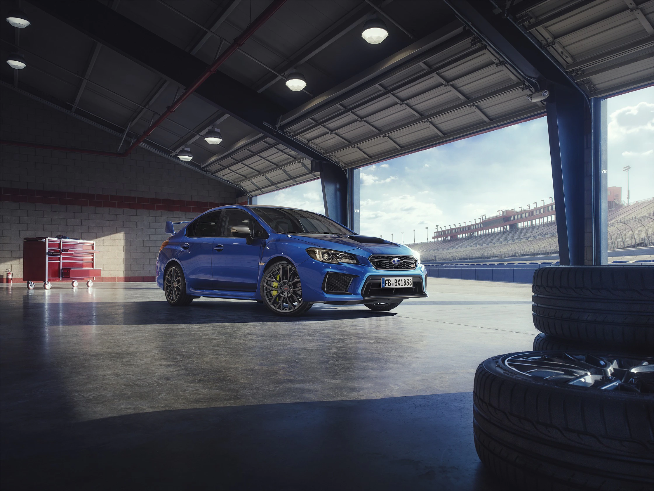 Ein blauer Sportwagen steht in einer Garage mit Blick auf eine Rennstrecke. Ersatzreifen sind im Vordergrund sichtbar.