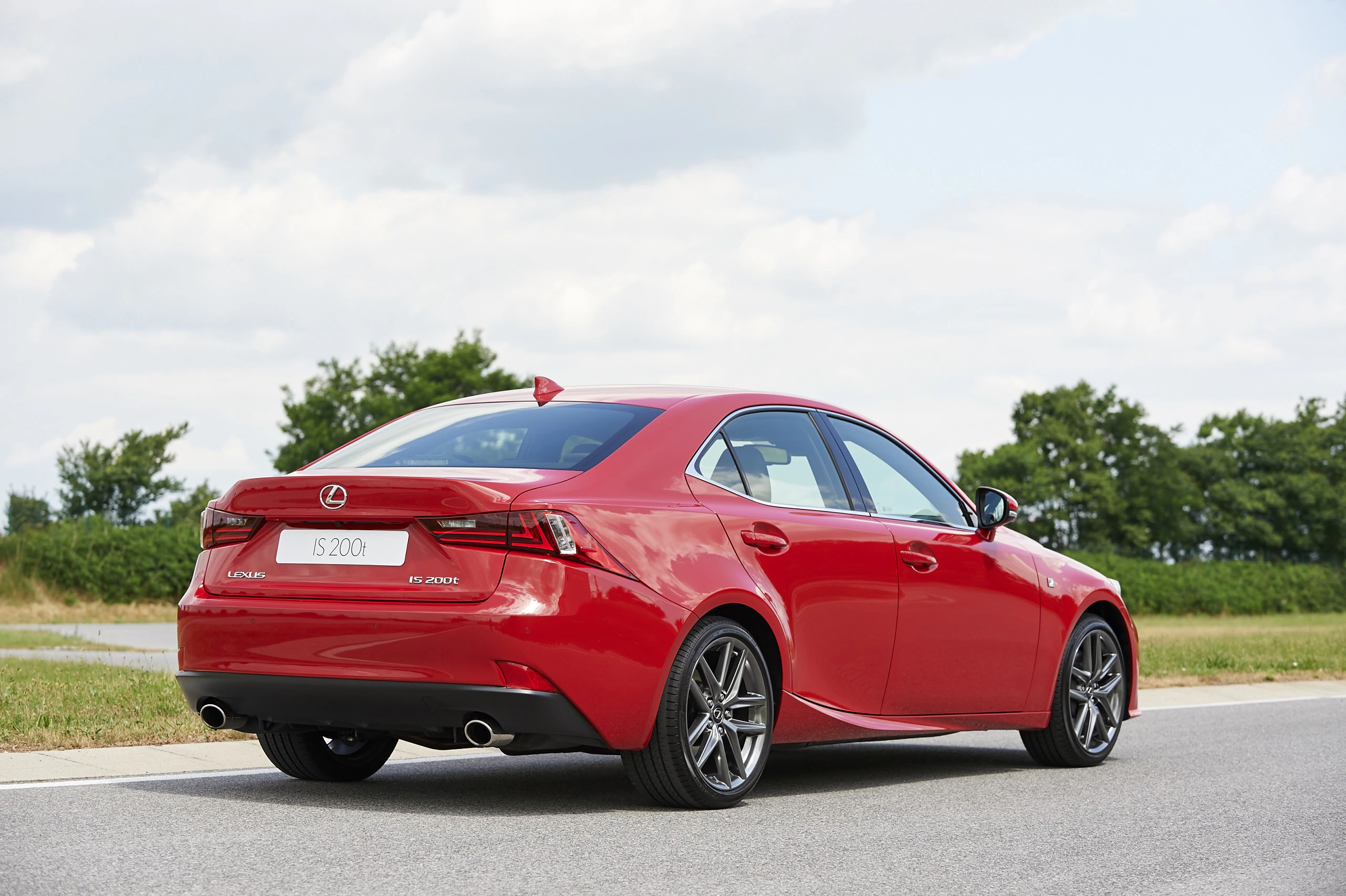 Roter Lexus IS 200t auf Landstraße, von hinten fotografiert. Bewölkter Himmel und grüne Bäume im Hintergrund.