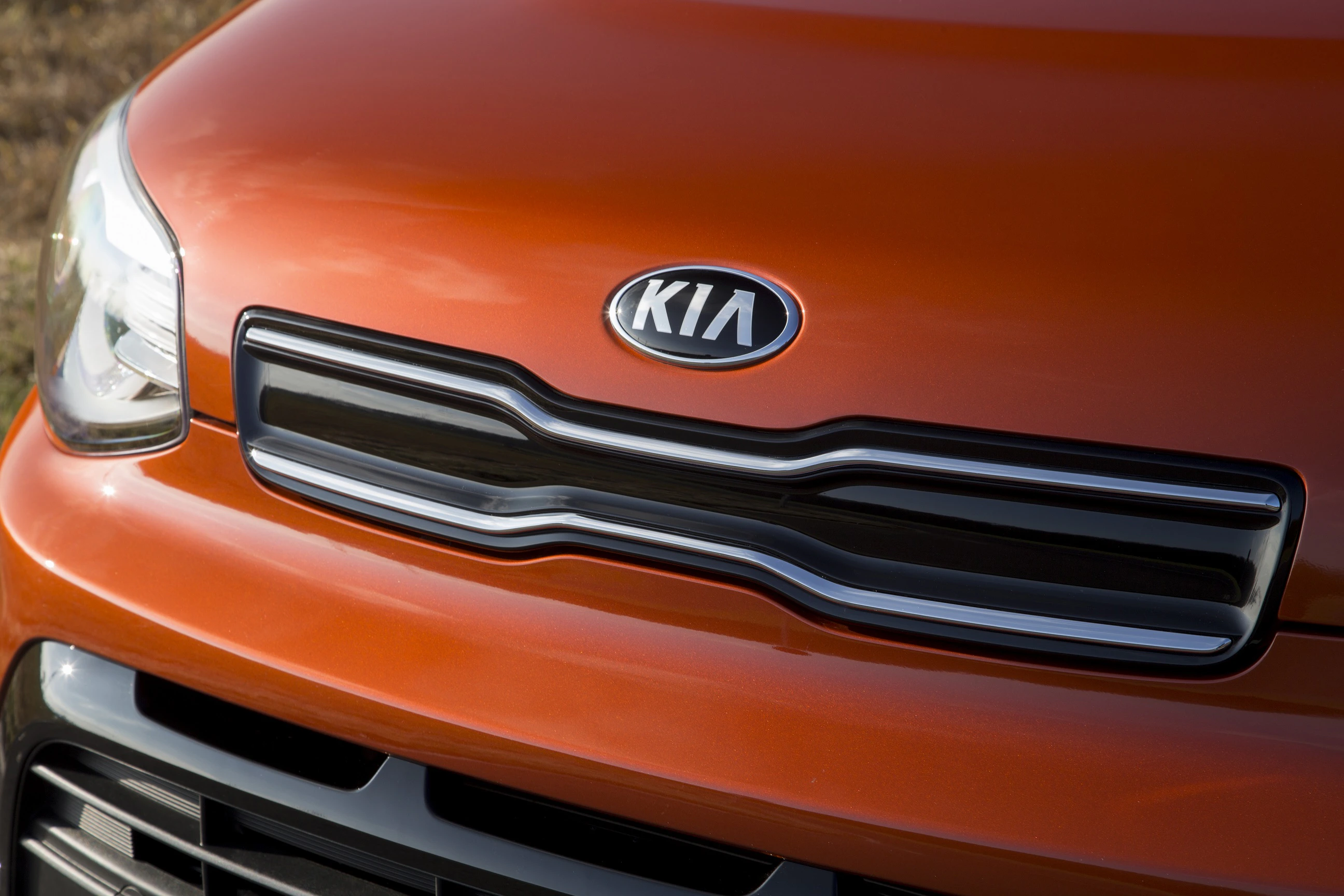 Nahaufnahme eines orangefarbenen Kia-Autos mit schwarzem Kühlergrill und silbernem Kia-Logo auf der Motorhaube.
