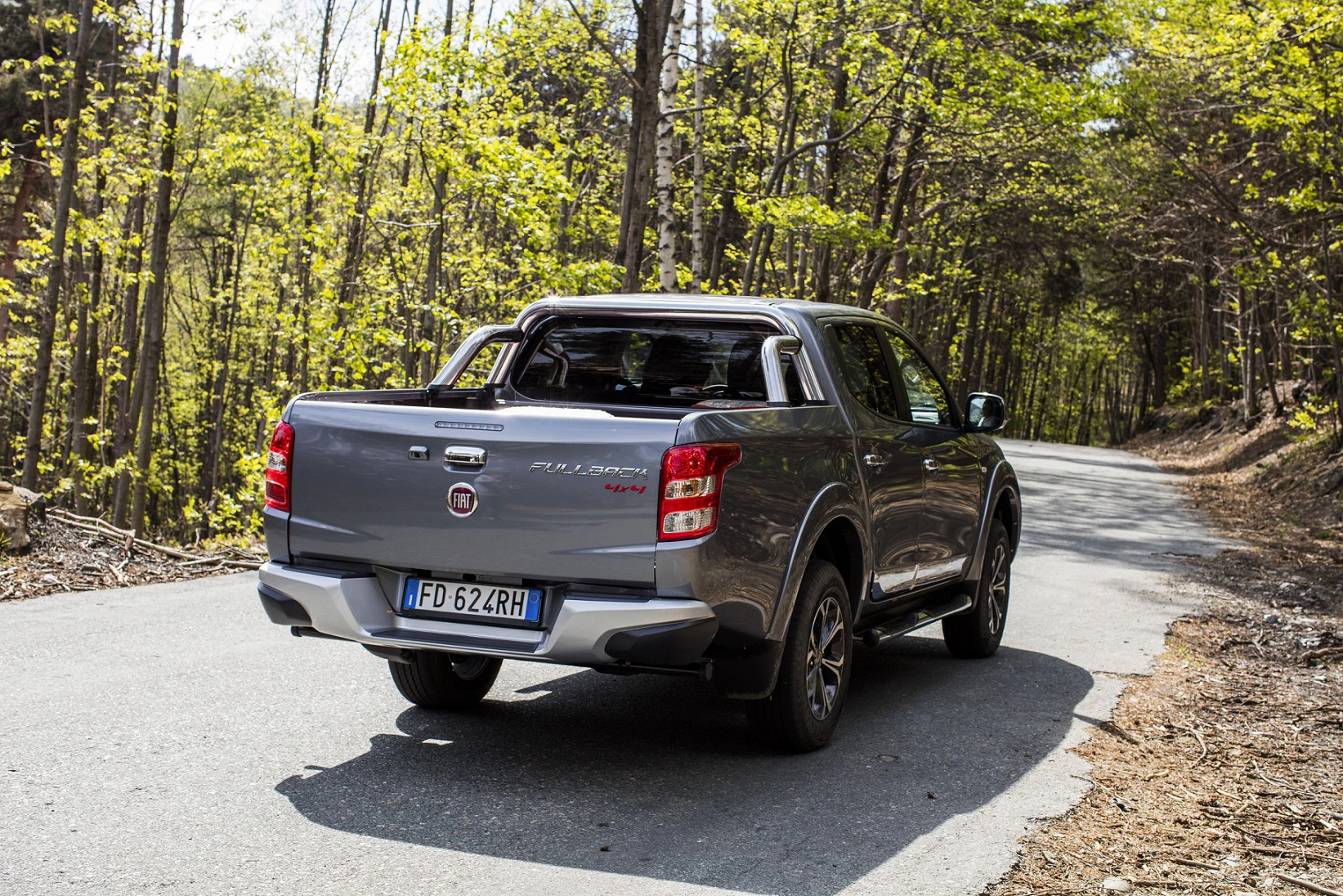 Grauer Fiat Fullback Pick-up fährt auf einer schmalen, von Bäumen gesäumten Landstraße. Kennzeichen aus Italien sichtbar.