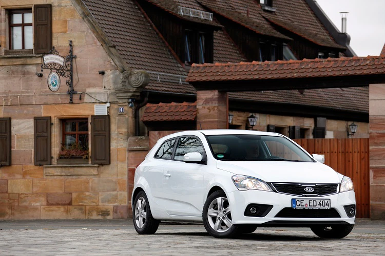 Weißes Auto parkt vor einem traditionellen Gebäude mit Fachwerk und steinerner Fassade.