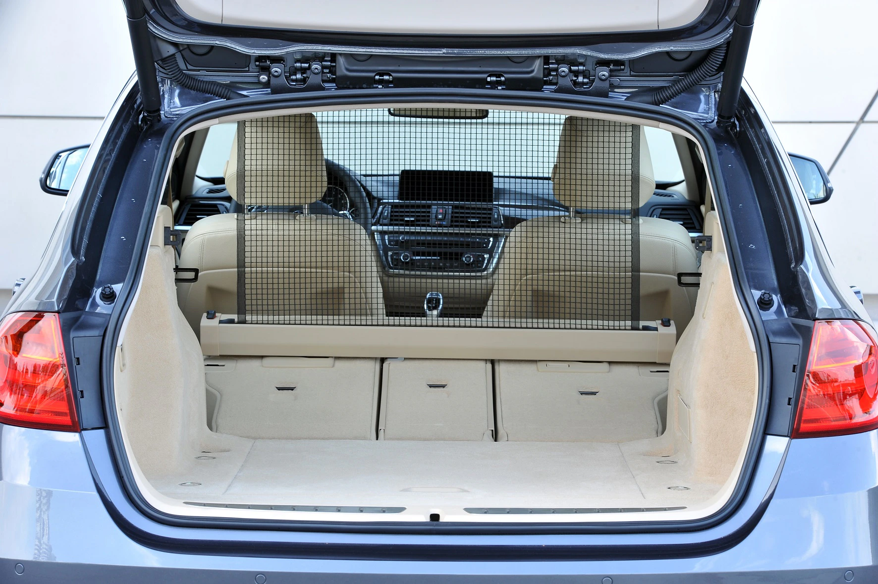 Blick in den Kofferraum eines Autos mit heruntergeklappten Rücksitzen und einem Schutzgitter, beige Innenraum.