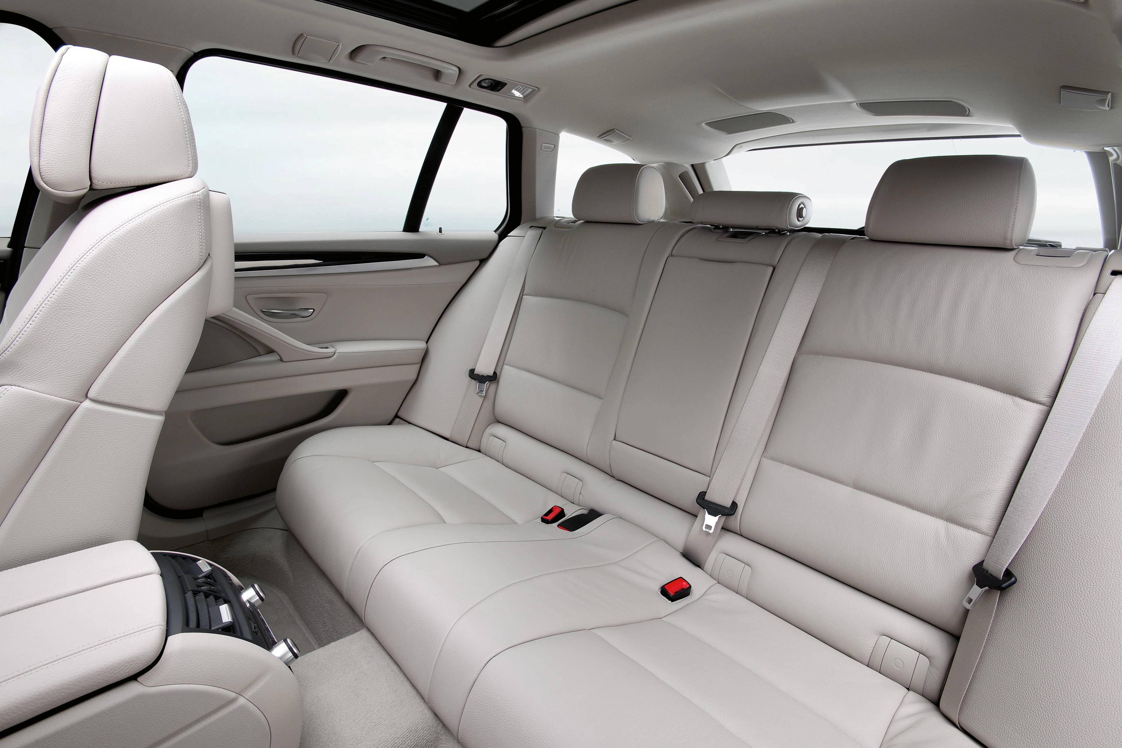Innenraum eines Autos mit beigen Ledersitzen, geräumige Rückbank, Kopfstützen und Sicherheitsgurte, moderne Ausstattungsdetails sichtbar.