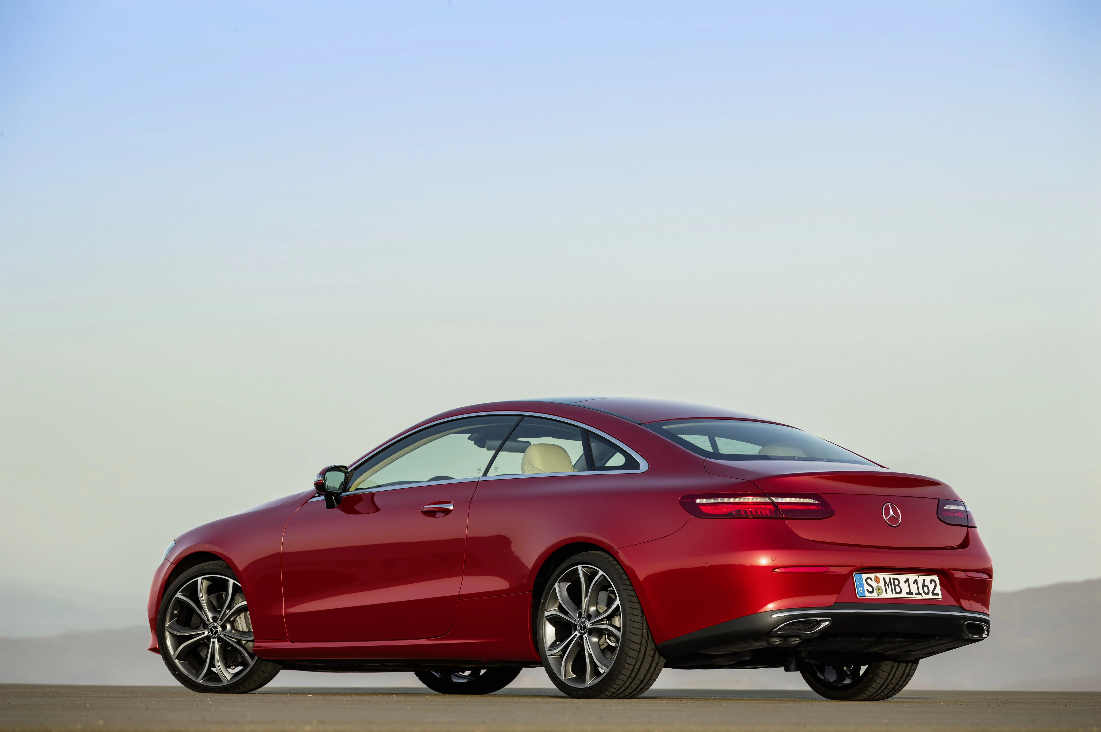 Rotes Mercedes-Benz Coupé steht auf einer Ebene. Die Sonne spiegelt sich auf der glänzenden Karosserie. Blauer Himmel im Hintergrund.