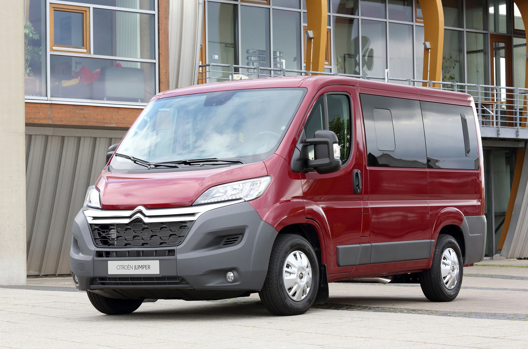 Roter Citroën Jumper Kleinbus geparkt vor einem modernen Gebäude mit großen Fenstern und Balkonen.