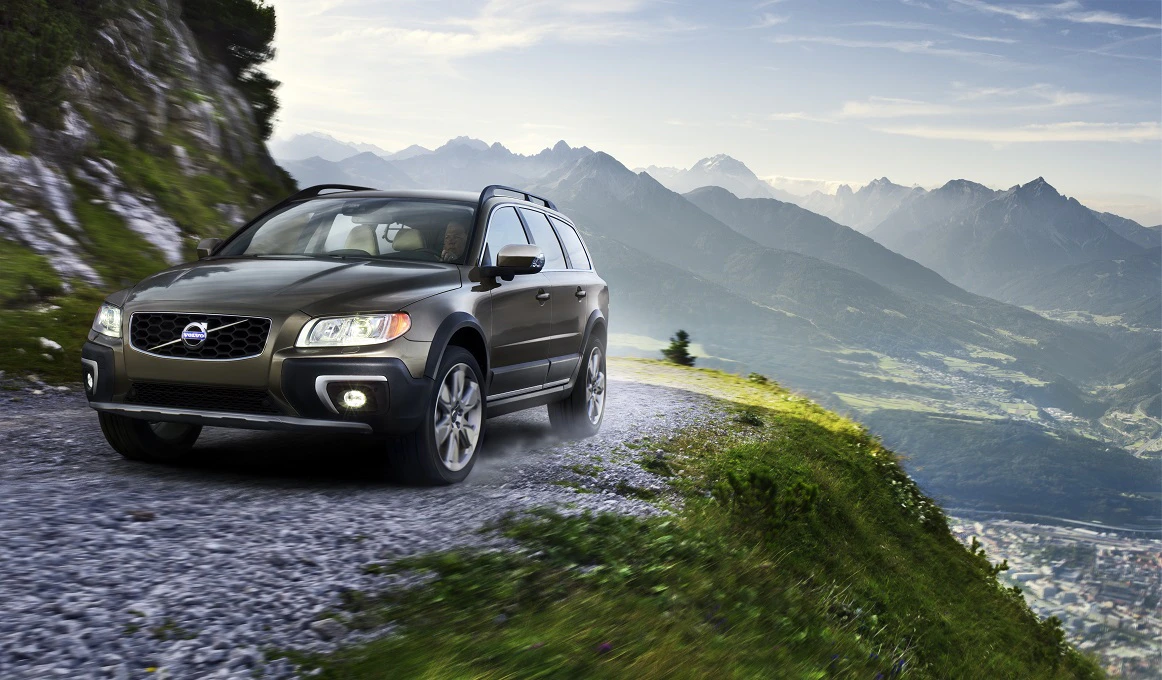 SUV fährt auf einer kurvigen Bergstraße mit Alpenpanorama im Hintergrund.