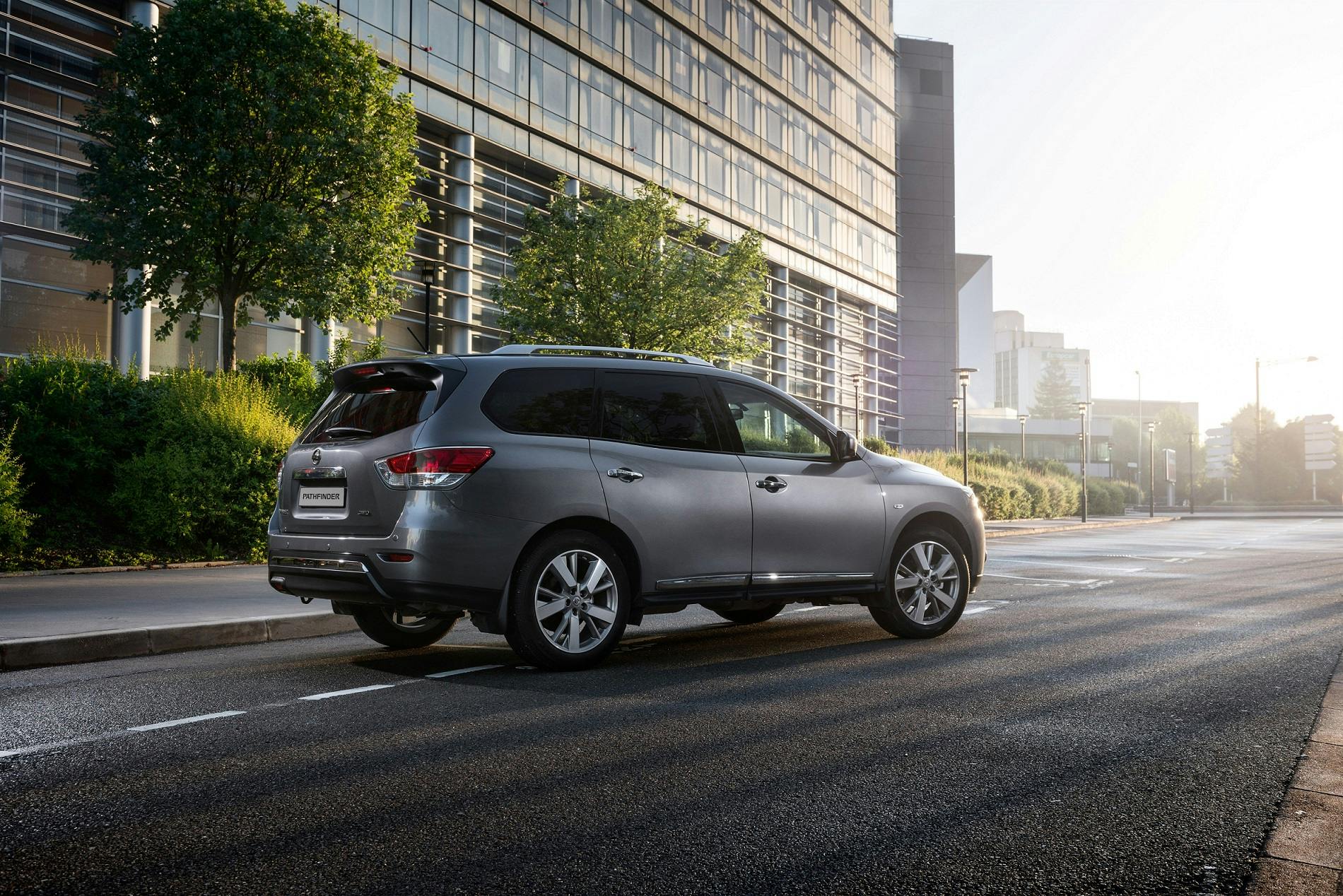 Silberner SUV parkt in einer modernen, städtischen Umgebung auf der Straße. Im Hintergrund sind Büros und Bäume zu sehen.
