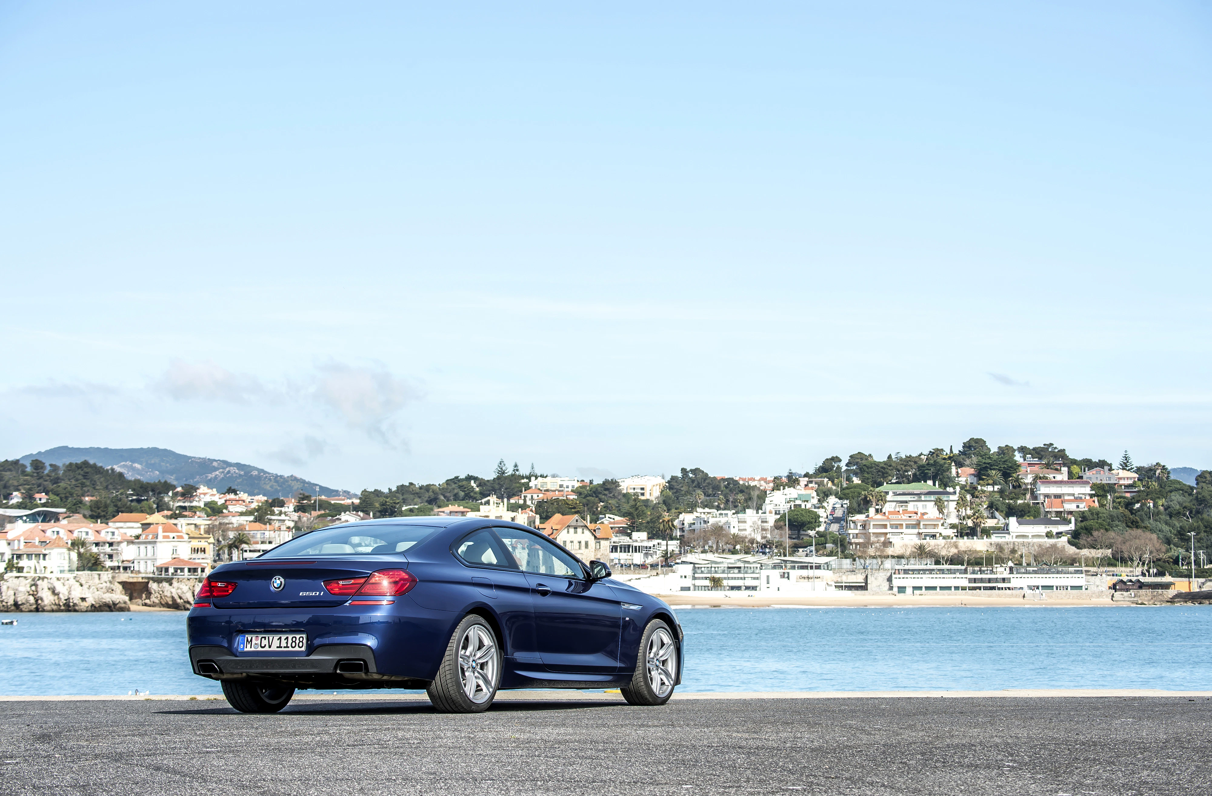 Blaues Auto am Hafen mit Blick auf die Stadt im Hintergrund, unter klarem Himmel und sonnigem Wetter.
