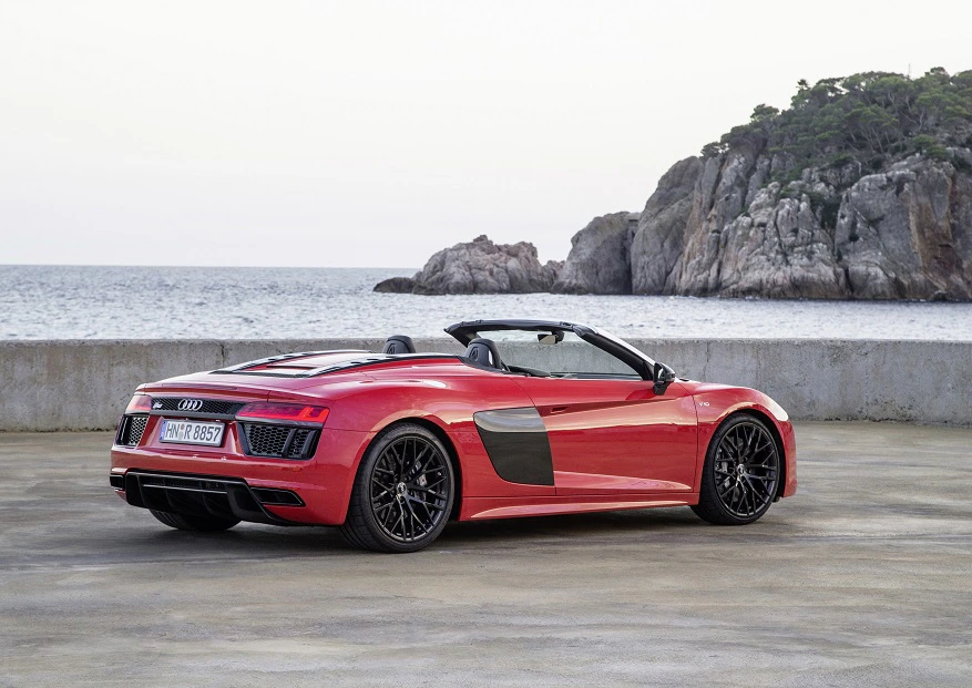 Roter Audi R8 Cabrio parkt auf einer Küstenstraße mit Blick aufs Meer und eine Felsformation im Hintergrund.