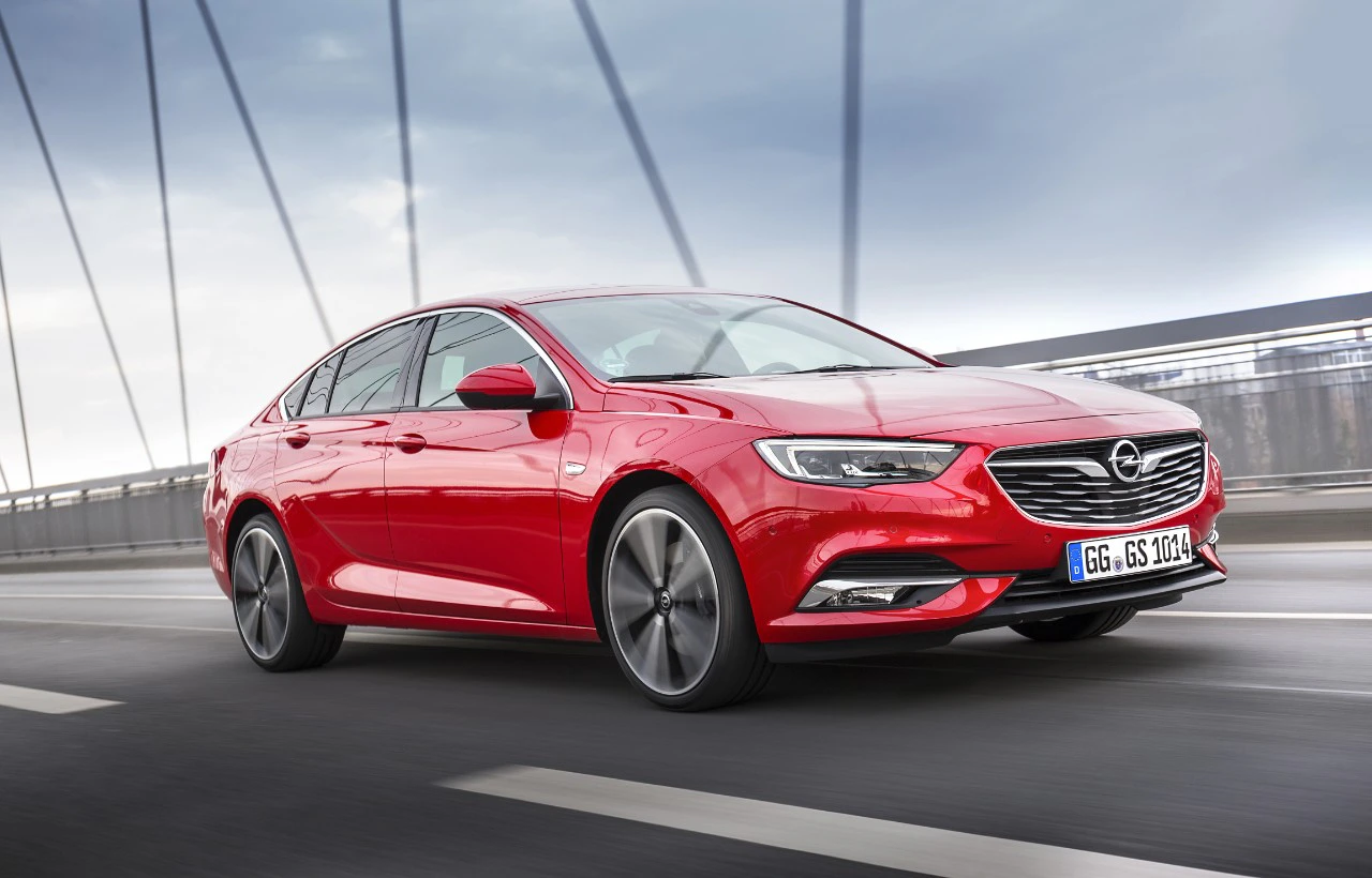 Rotes Auto, Modell Opel Insignia, fährt auf einer Brücke bei bewölktem Himmel. Sicht auf die rechte Seite und Front des Wagens.
