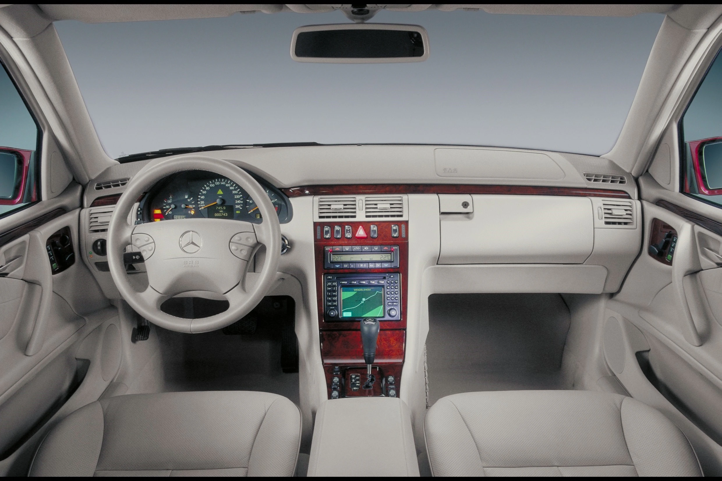 Innenraum eines Autos mit grauem Leder, Holzverkleidung und modernem Armaturenbrett mit Navigationssystem. Mercedes-Logo auf dem Lenkrad.