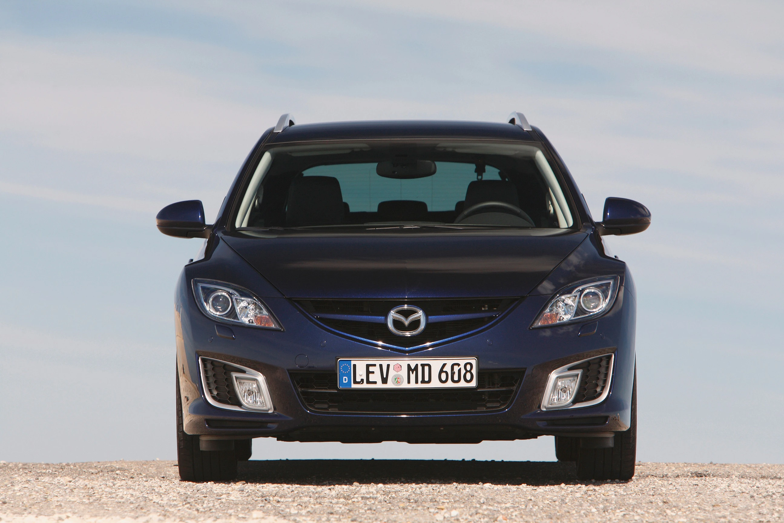 Blauer Mazda CX-7 von vorne auf einer Straße, blauer Himmel im Hintergrund.