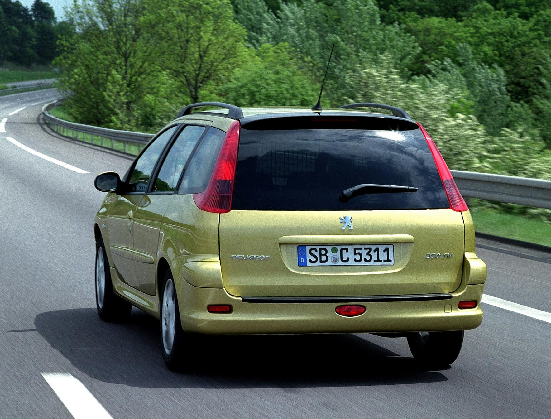 Ein gelber Peugeot Kombi fährt auf einer Landstraße, umgeben von grüner Natur und Bäumen.