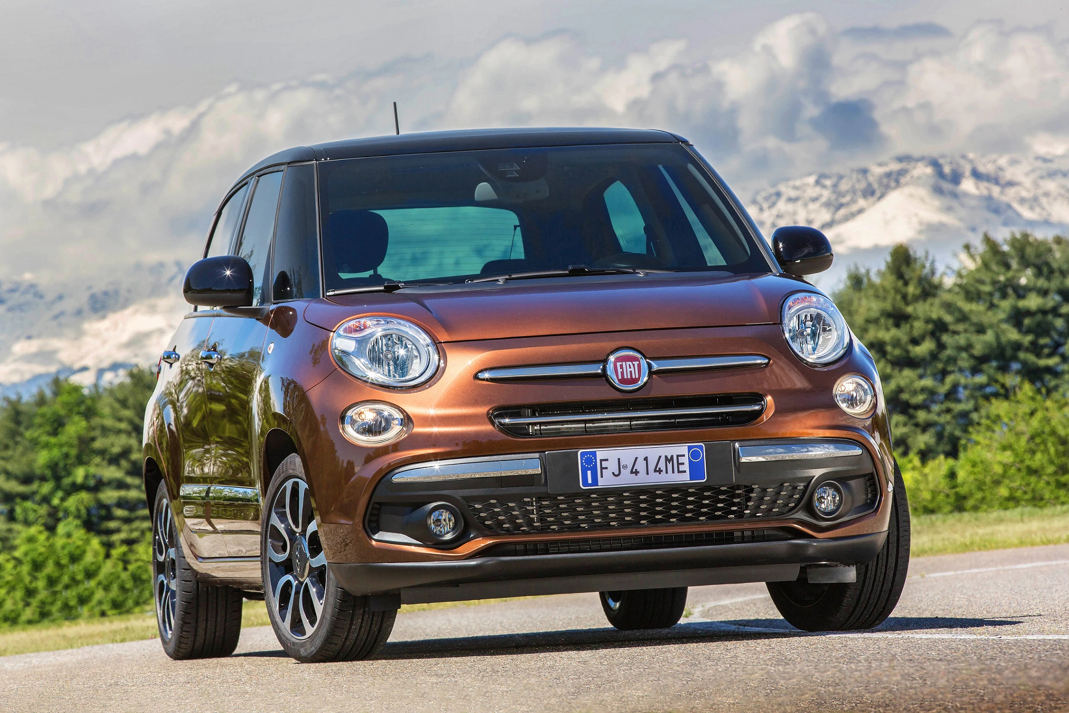 Brauner Fiat 500L auf einer Straße vor einer malerischen Berglandschaft bei klarem Himmel.