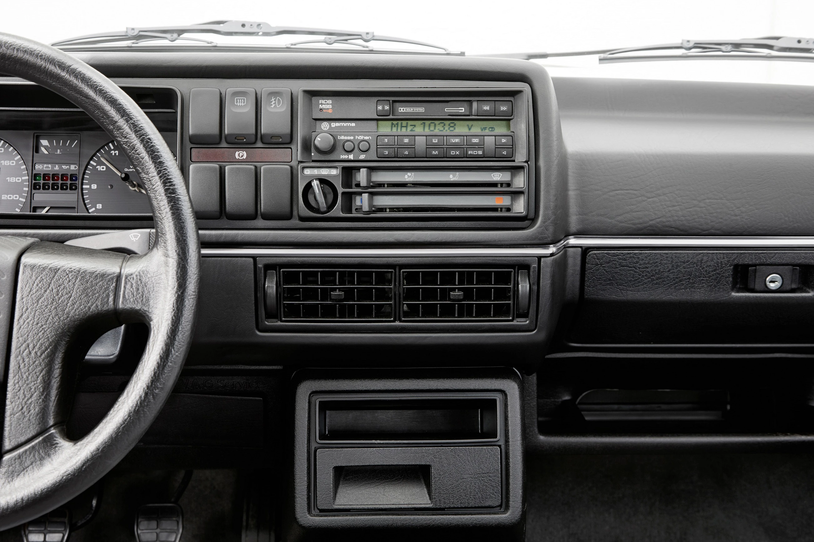 Armaturenbrett eines älteren Autos mit Lenkrad, Tacho und Radio in der Mittelkonsole, darunter Lüftungsschlitze und Ablagefächer.