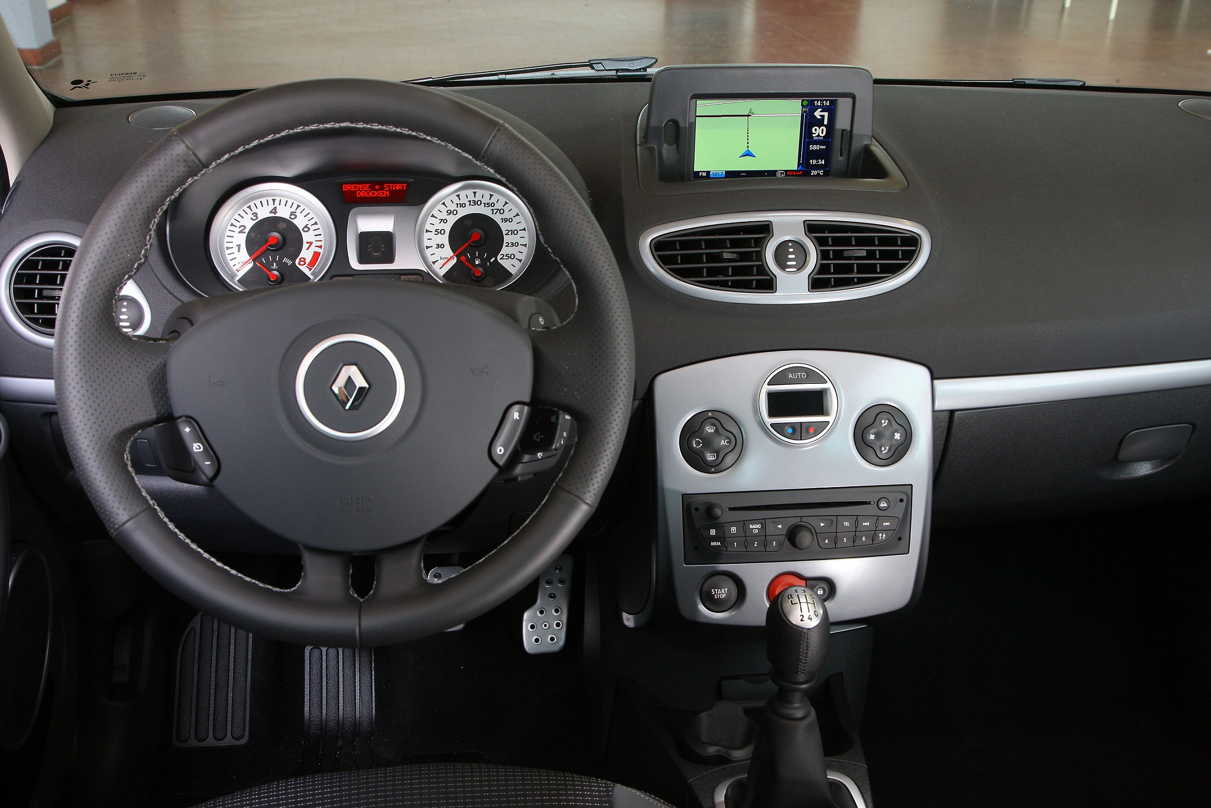 Innenraum eines Autos mit Renault-Logo am Lenkrad, Armaturenbrett mit Tachometern, Navigationssystem und Schalthebel.