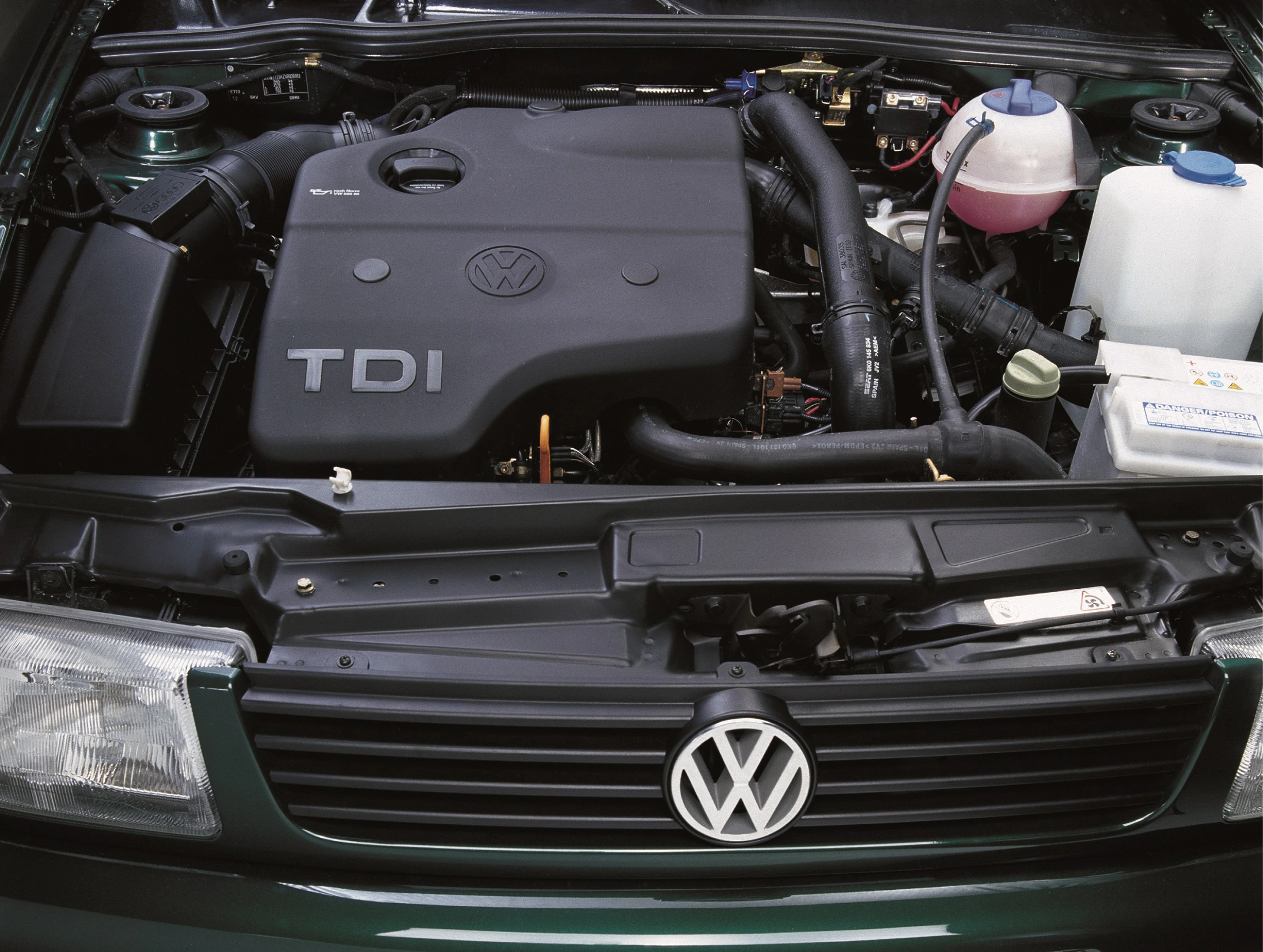 Motorraum eines Volkswagen mit TDI-Motor. Deutlich sichtbar sind das VW-Logo, der Motorblock und verschiedene Behälter und Schläuche.
