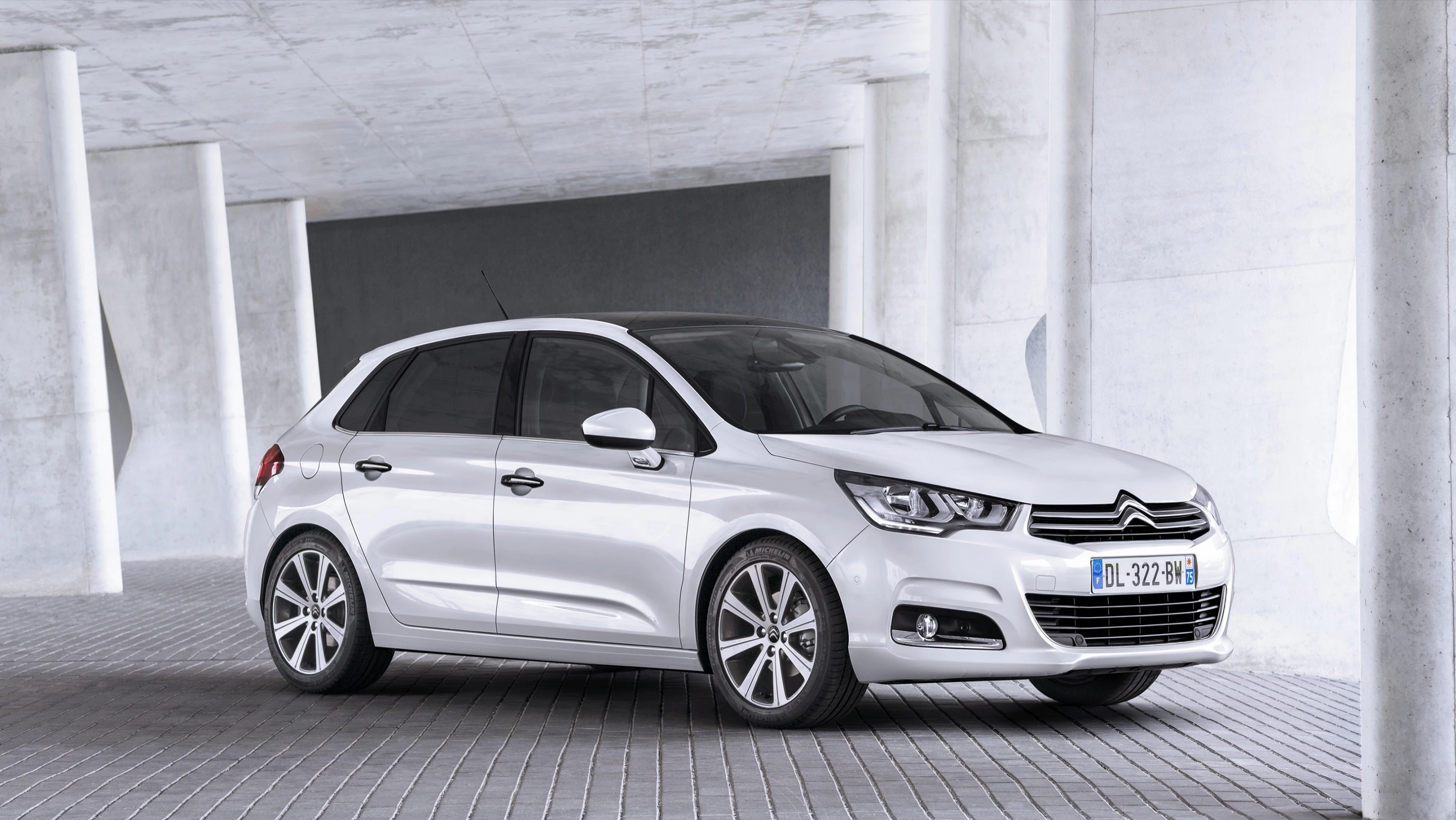 Weißer Citroën C4 geparkt auf grauem Pflaster unter einem modernen Betondach.