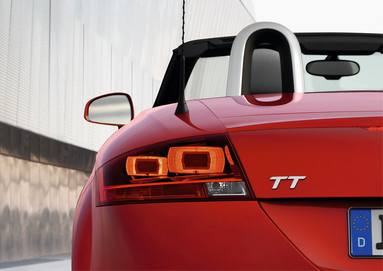 Roter Audi TT Roadster von hinten, Fokus auf Rückleuchte und Emblem, modernes Gebäude im Hintergrund.
